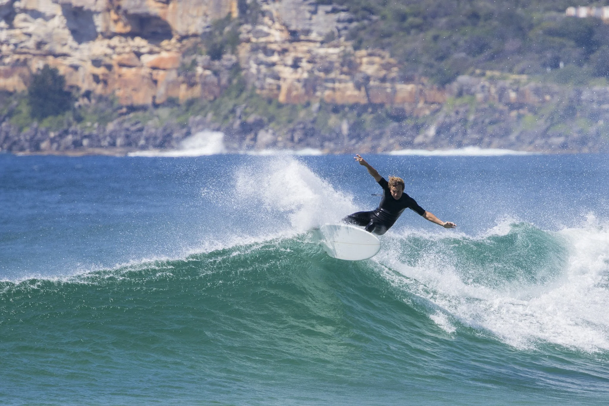 A person surfing on a wave in the ocean with rocky cliffs in the background.