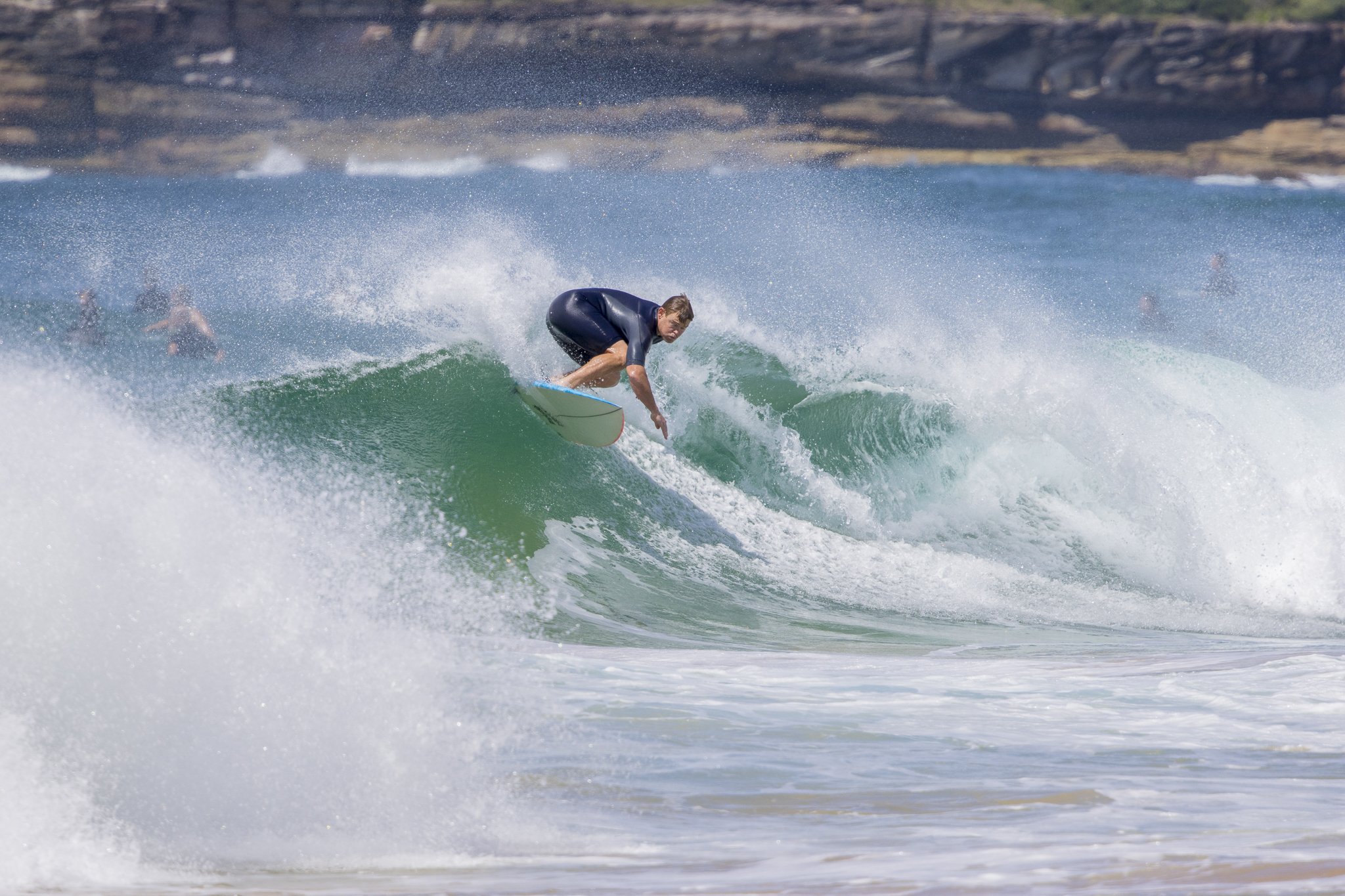 A surfer riding a green wave with several other surfers in the background at the beach.