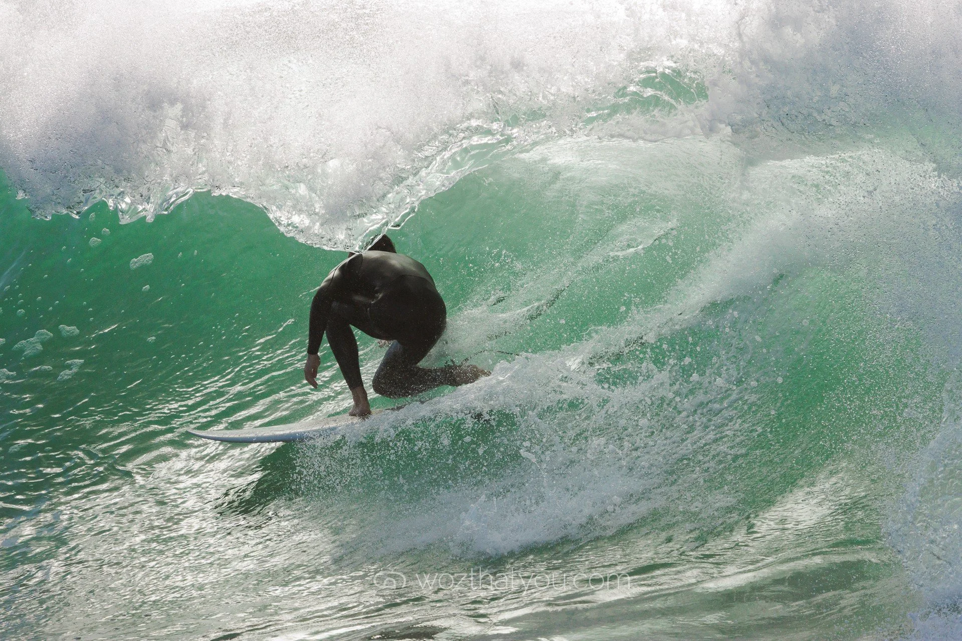 A surfer wearing a black wetsuit riding inside a green ocean wave.