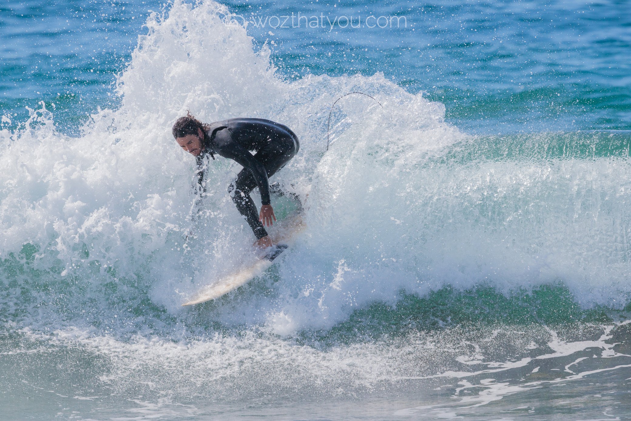 Person in a wetsuit riding a surfboard on a small wave at the beach.
