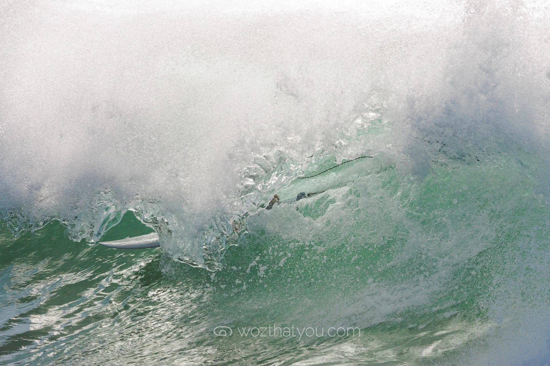 A surfer riding inside a wave, partially obscured by the water spray and foam.