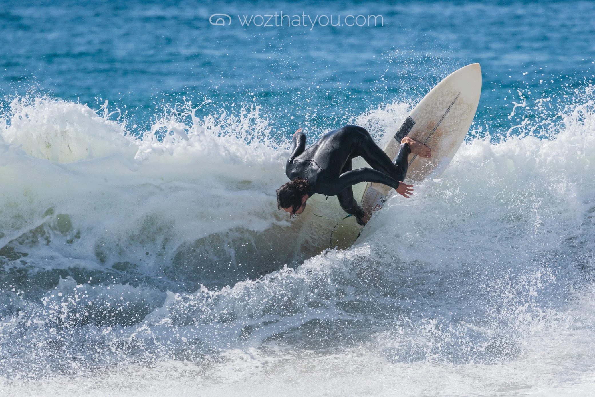 A surfer in a black wetsuit riding a wave on a surfboard in the ocean.