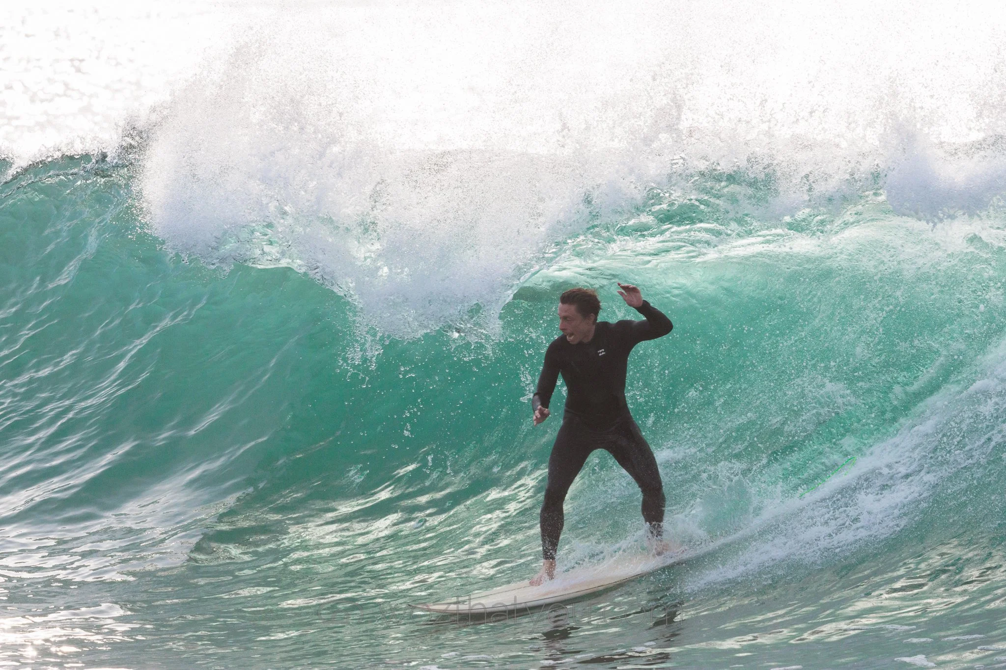 A person surfing on a large ocean wave with a wide smile, wearing a black wetsuit.