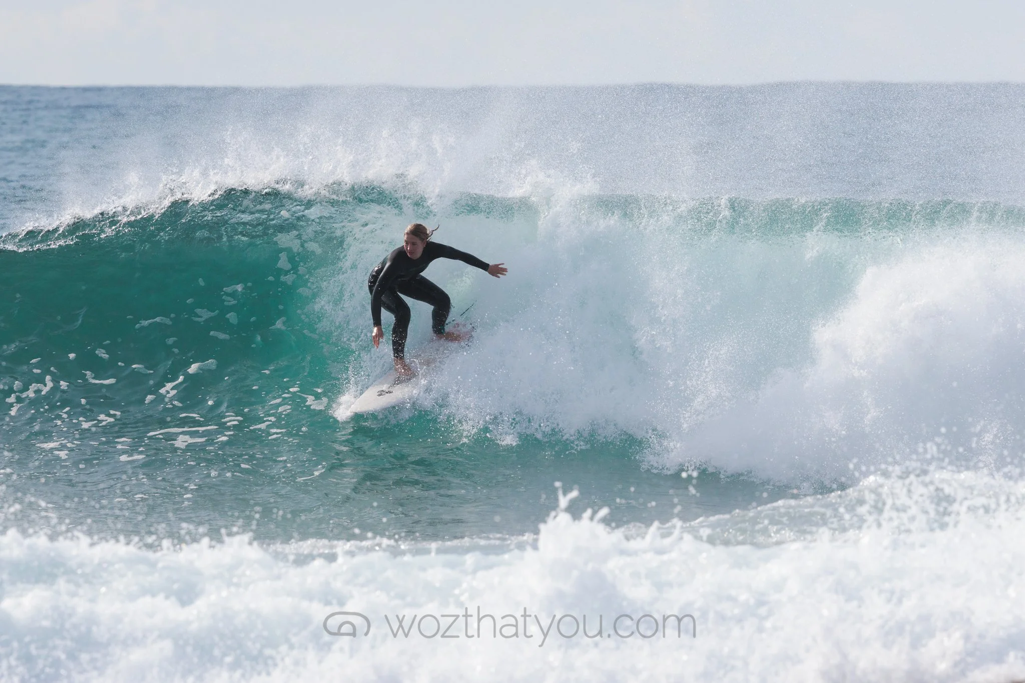 A woman surfing on a wave in the ocean, wearing a black wetsuit.