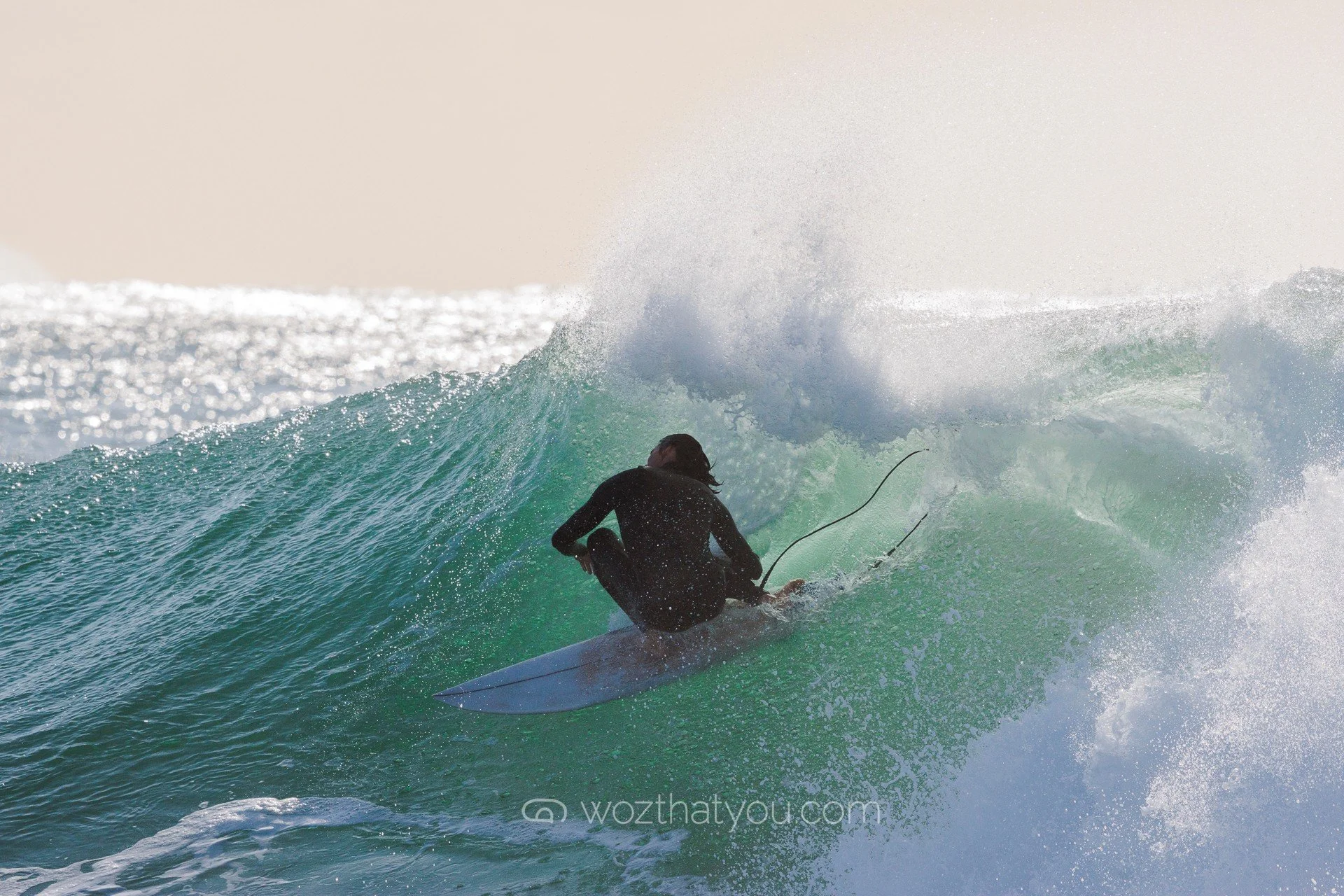 A person wearing a black wetsuit surfing on a green wave in the ocean.