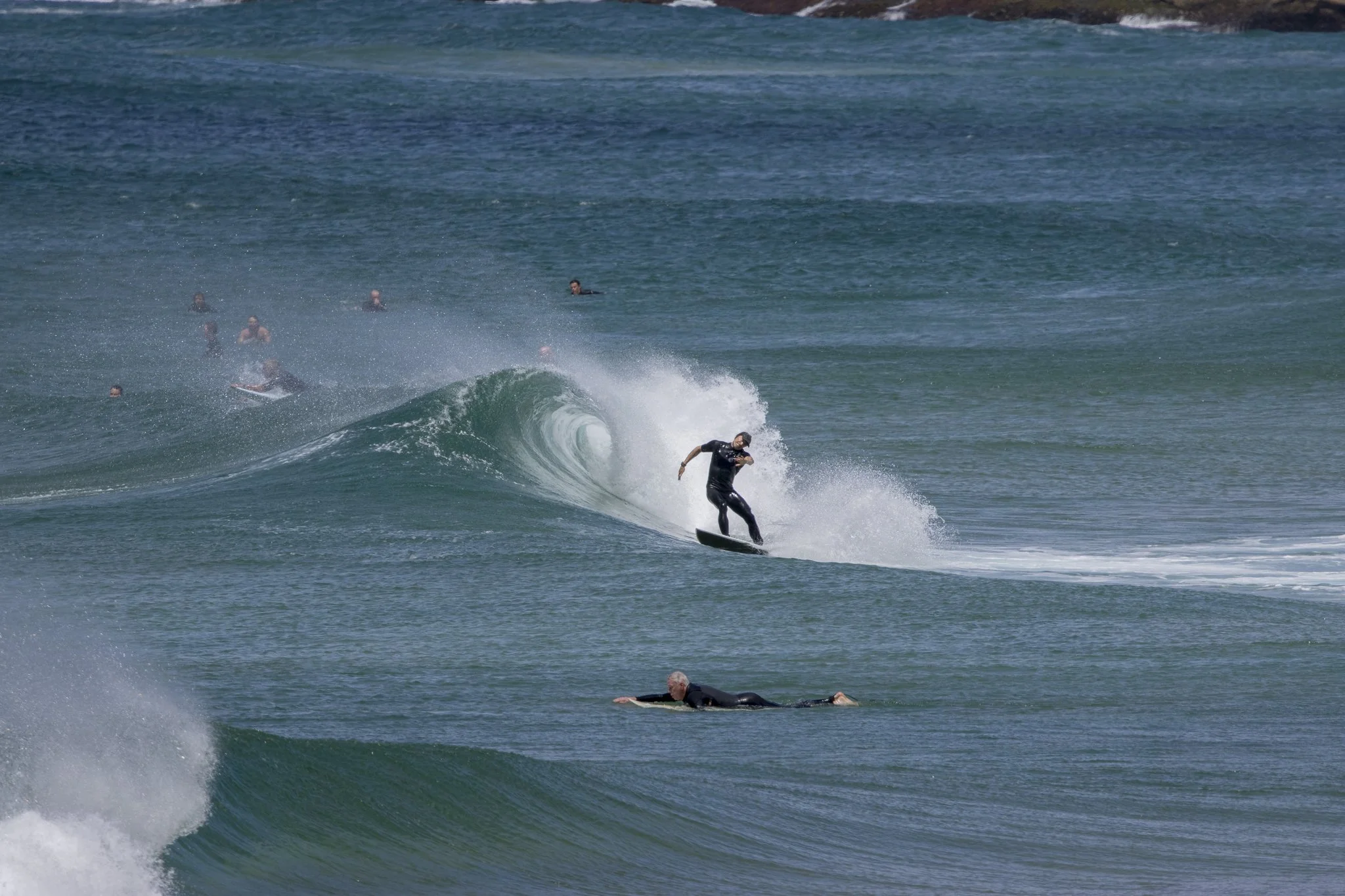 A person surfing on a wave with several other surfers in the water nearby.