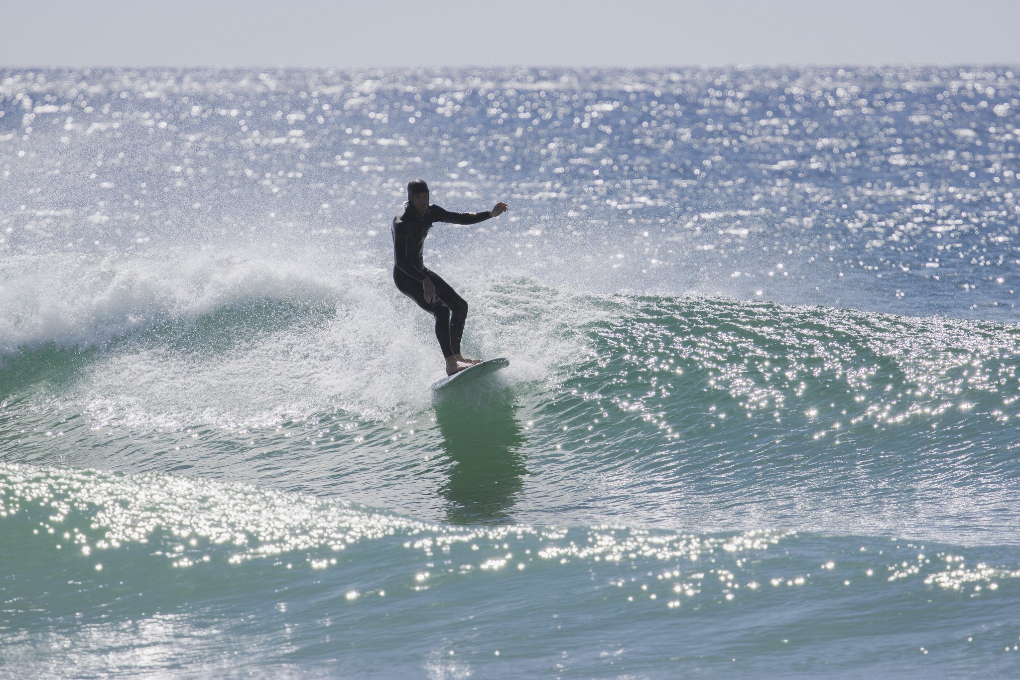 A person in a wetsuit surfing on a small wave in the ocean with sunlight reflecting off the water.