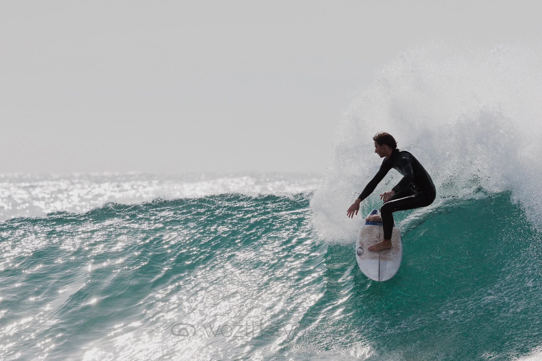 A surfer riding a wave in the ocean, wearing a black wetsuit.