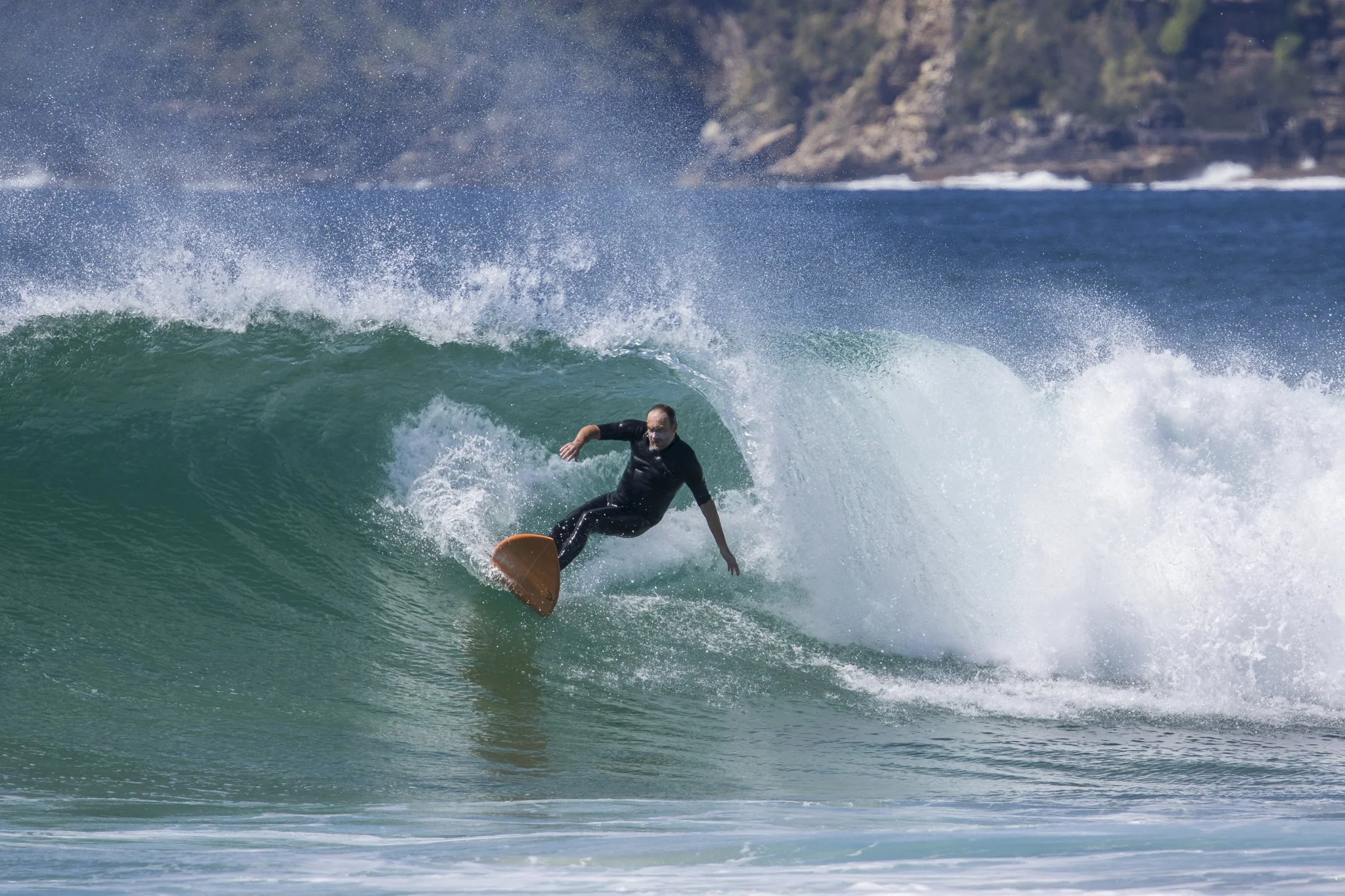 A person surfing on a wave in the ocean near a rocky coastline.