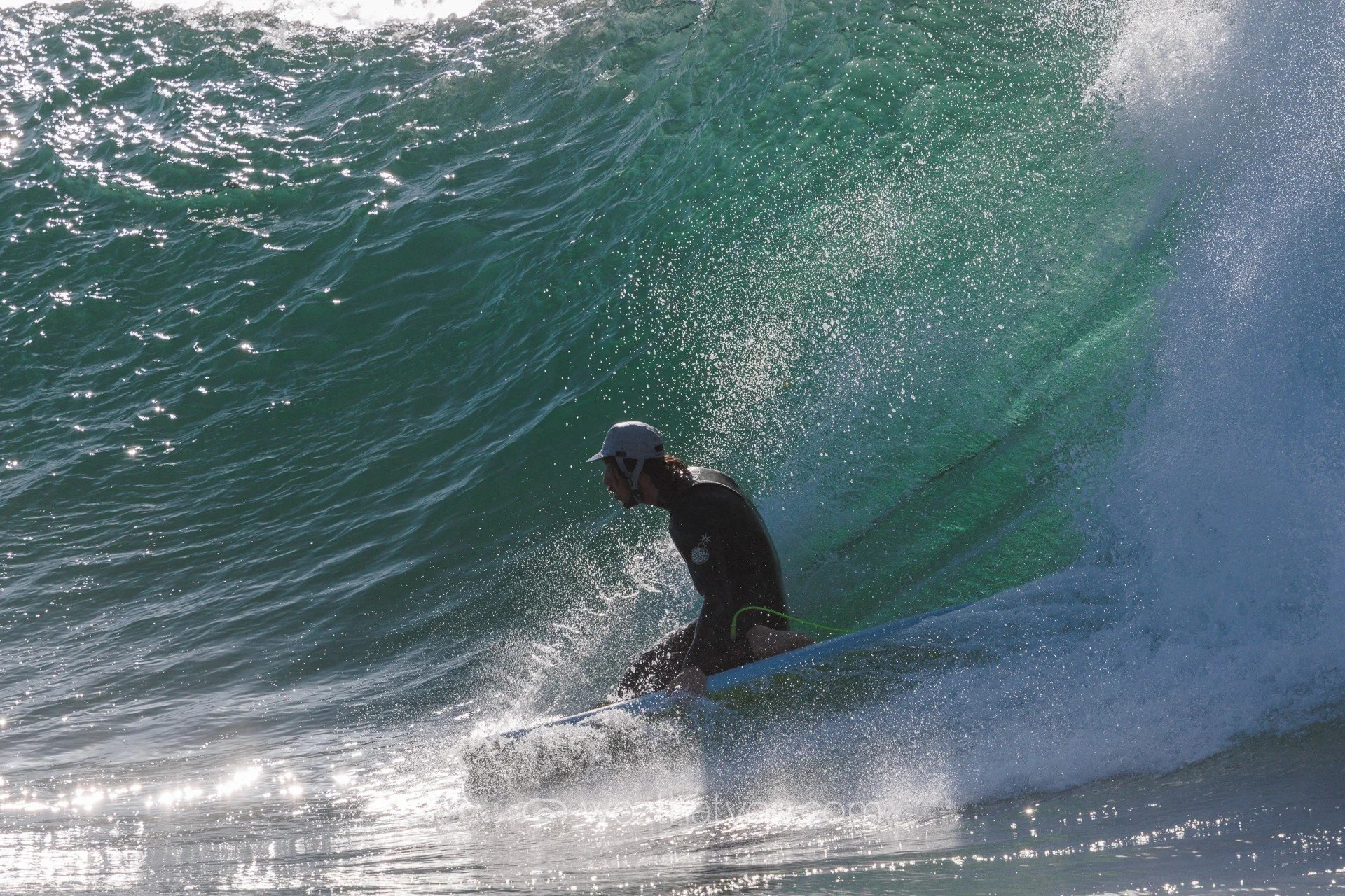 A person surfing on a wave in the ocean, wearing a helmet and wetsuit, with surfboard partially submerged.