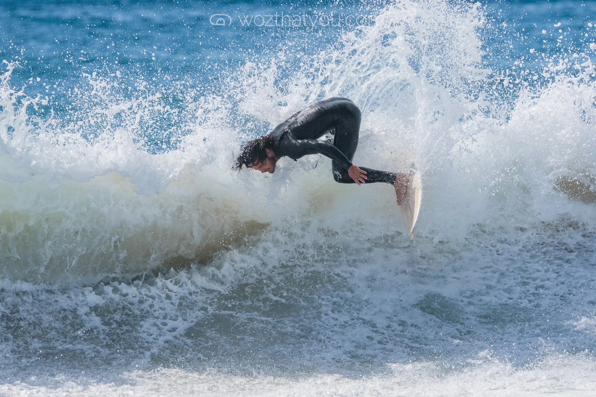 A person in a black wetsuit riding a wave on a surfboard in the ocean.