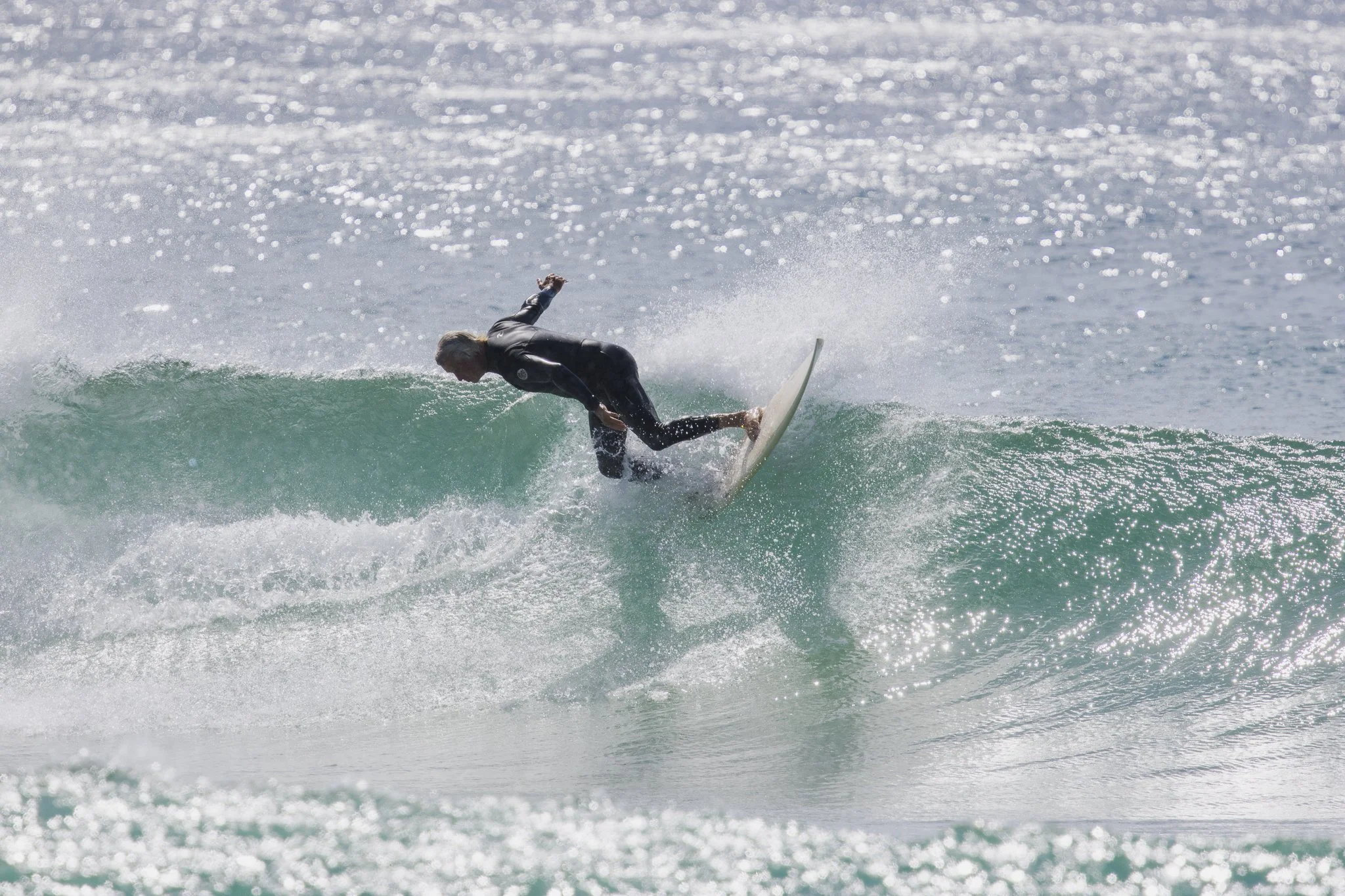A person wearing black wetsuit surfing on a small wave in the ocean.