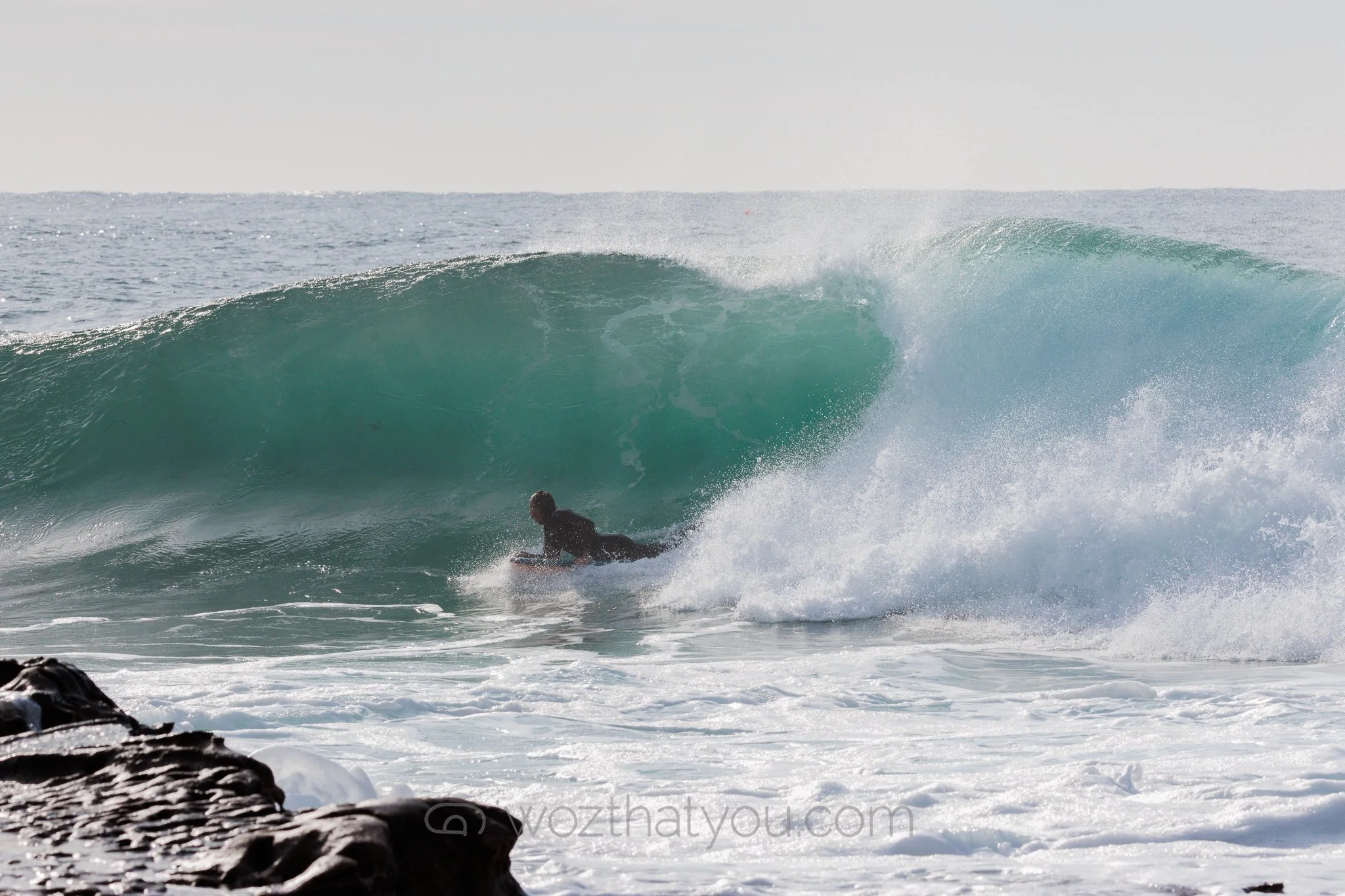 A person riding a surfboard inside the barrel of a breaking wave in the ocean.