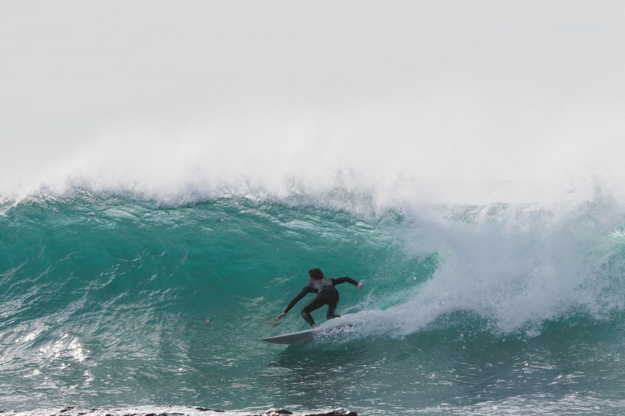 A person in a black wetsuit surfing on a large ocean wave.