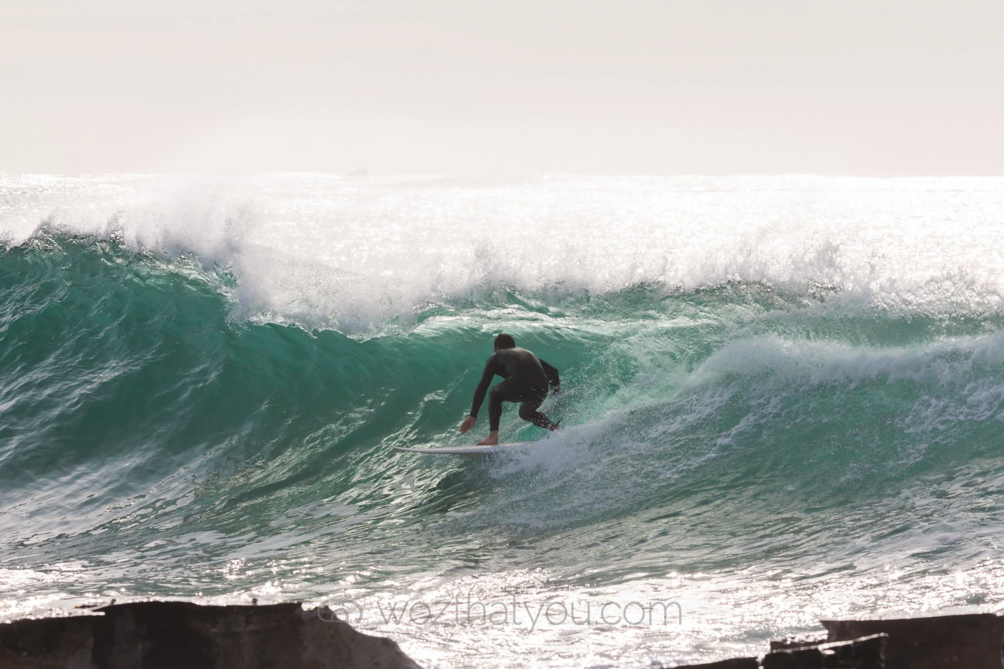 A person surfing on a wave at the beach, wearing a black wetsuit.
