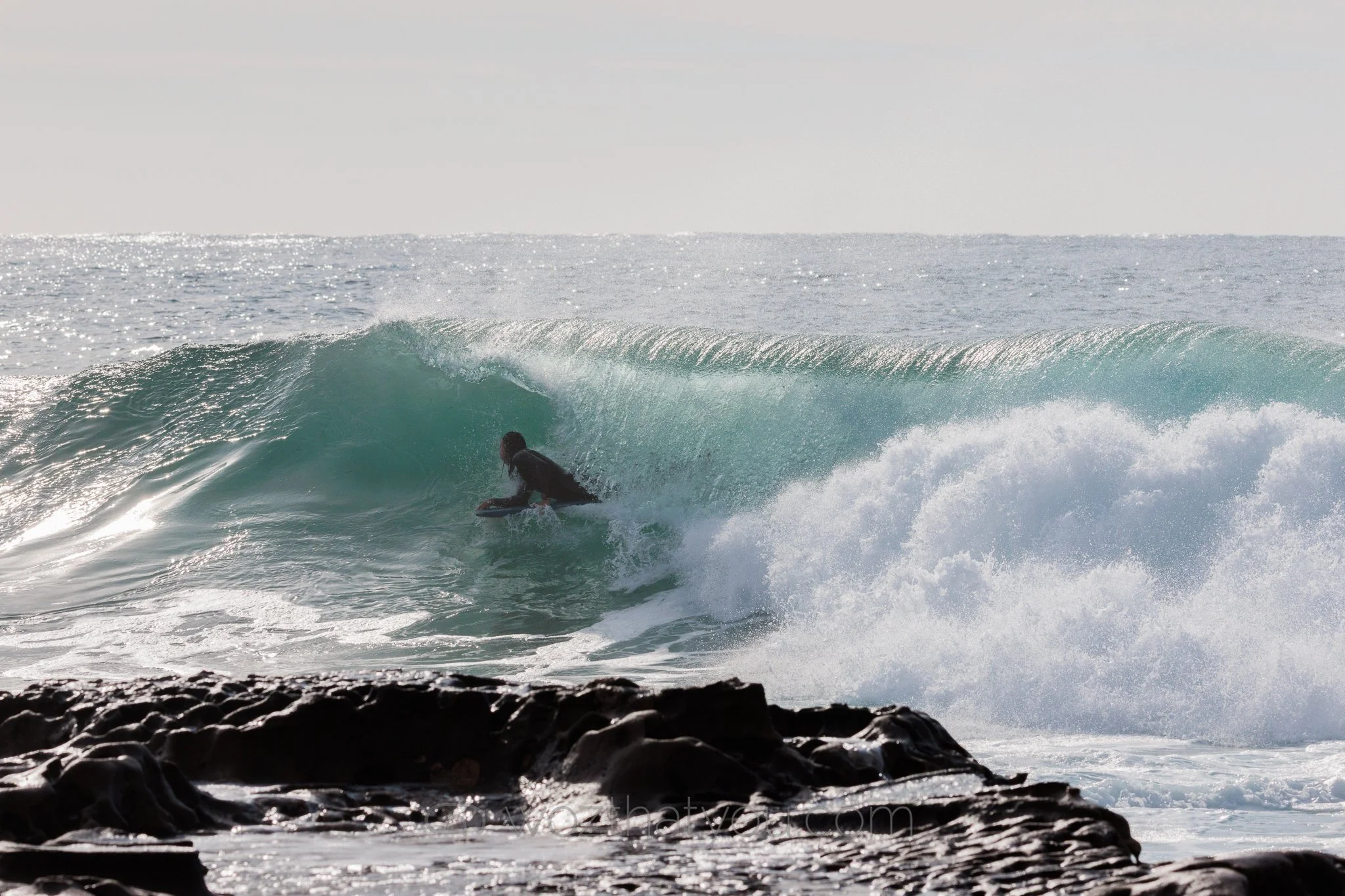 A person surfing on a wave near rocky shoreline during daytime.