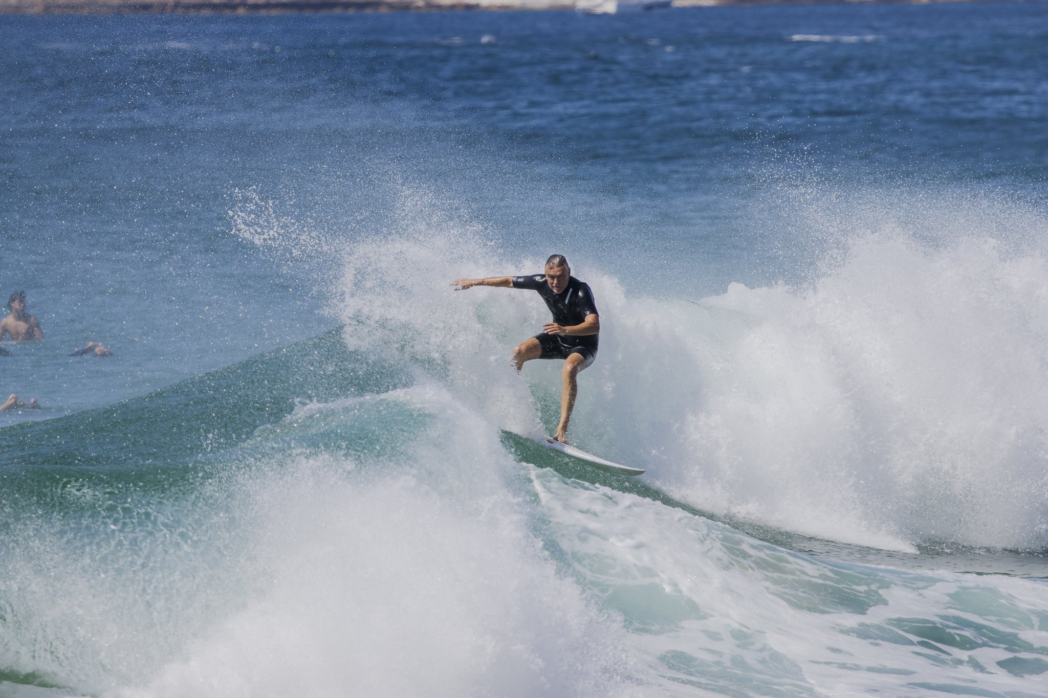 A person surfing on a wave in the ocean with other surfers in the background.