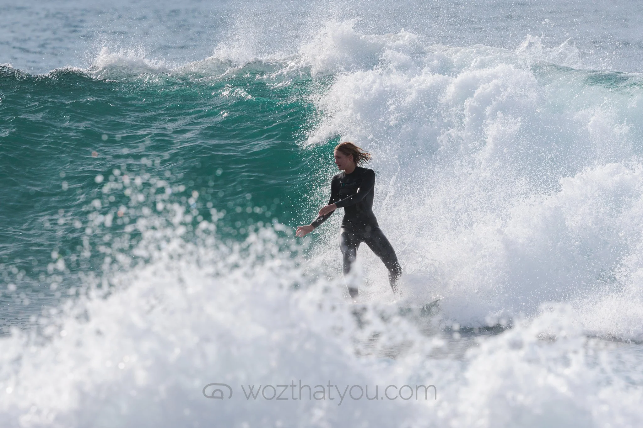 A female surfer in a black wetsuit riding a wave in the ocean.