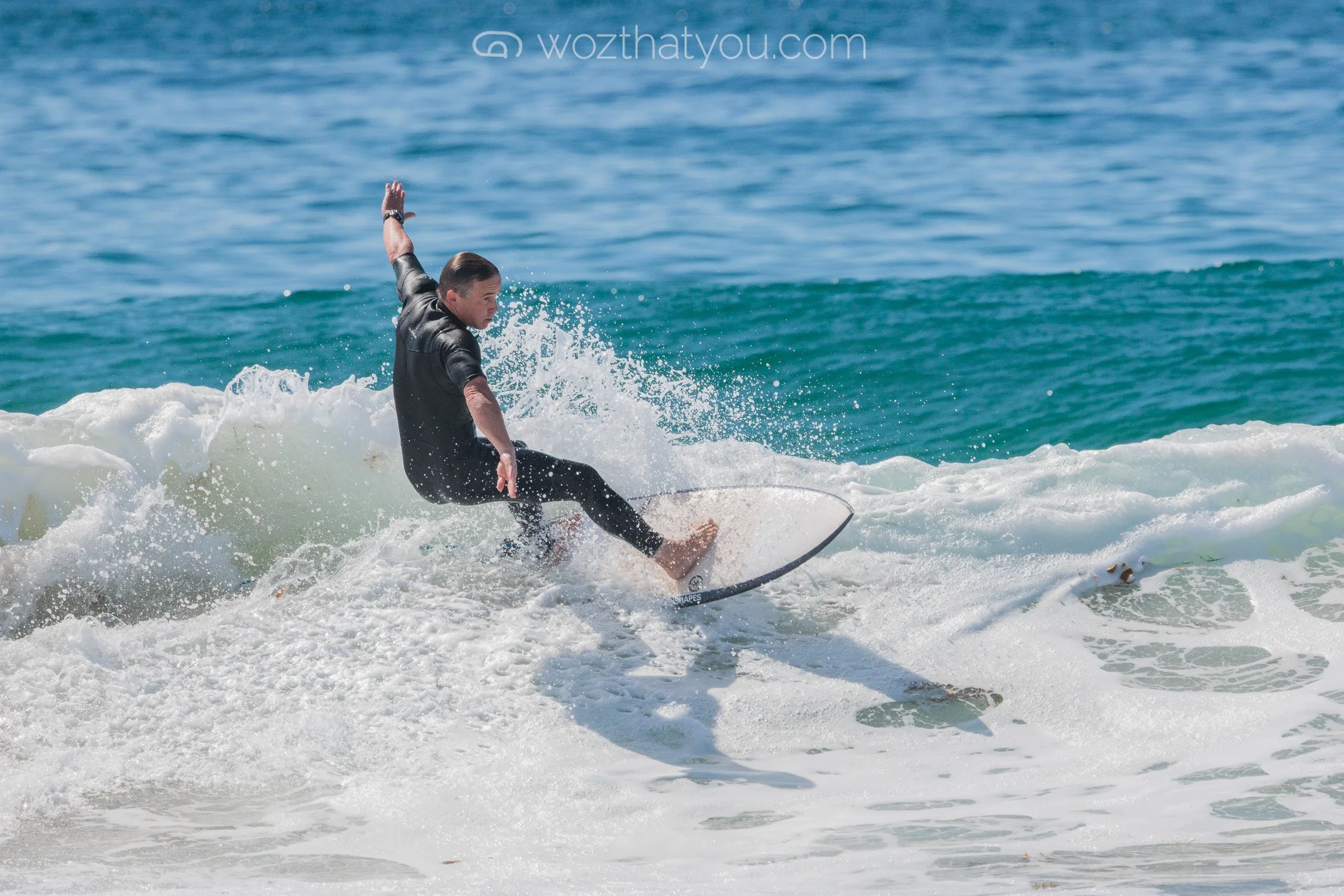 A person surfing on a wave in the ocean, wearing a black wetsuit.