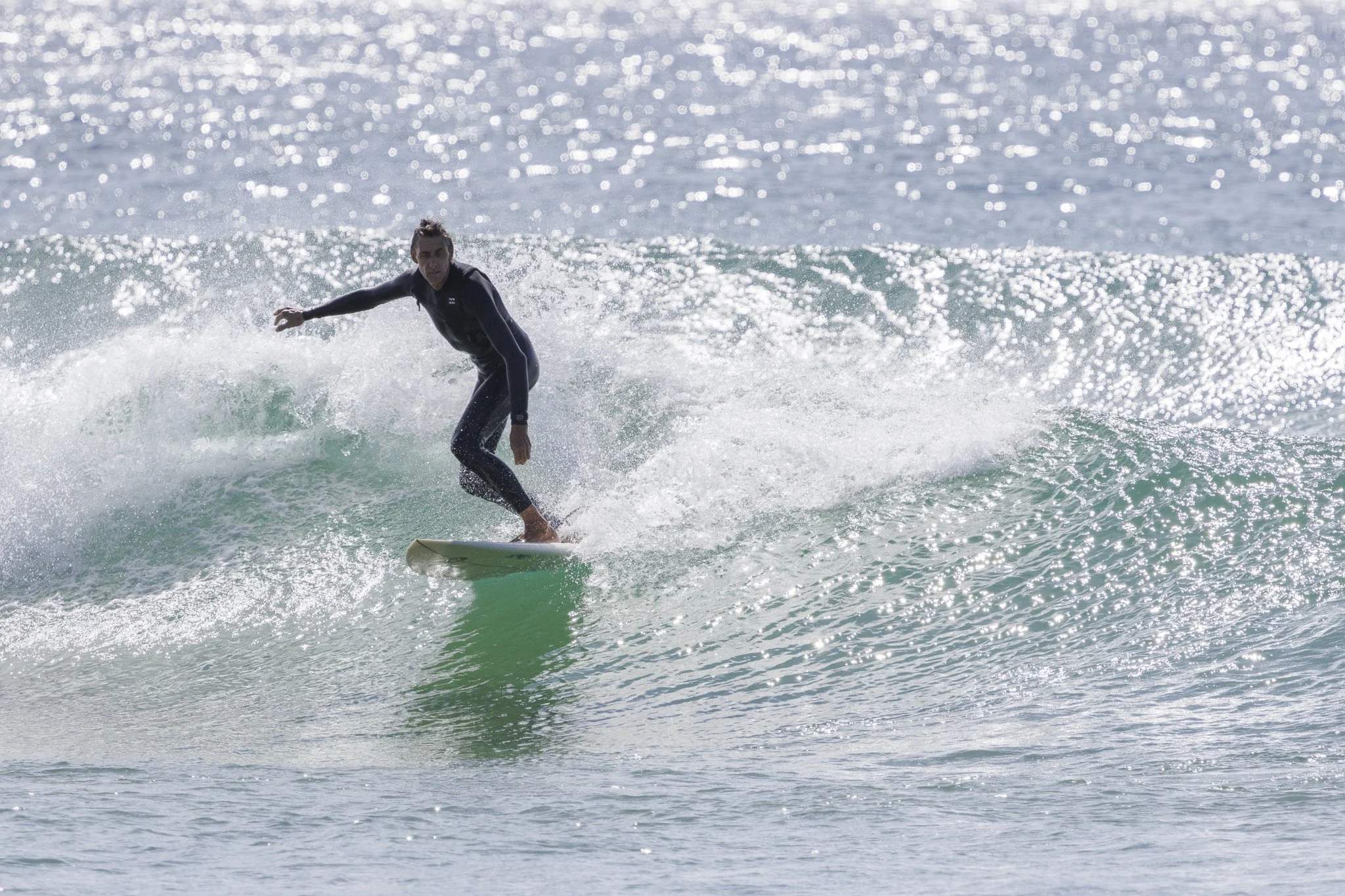 A person surfing on a wave in the ocean, wearing a black wetsuit.