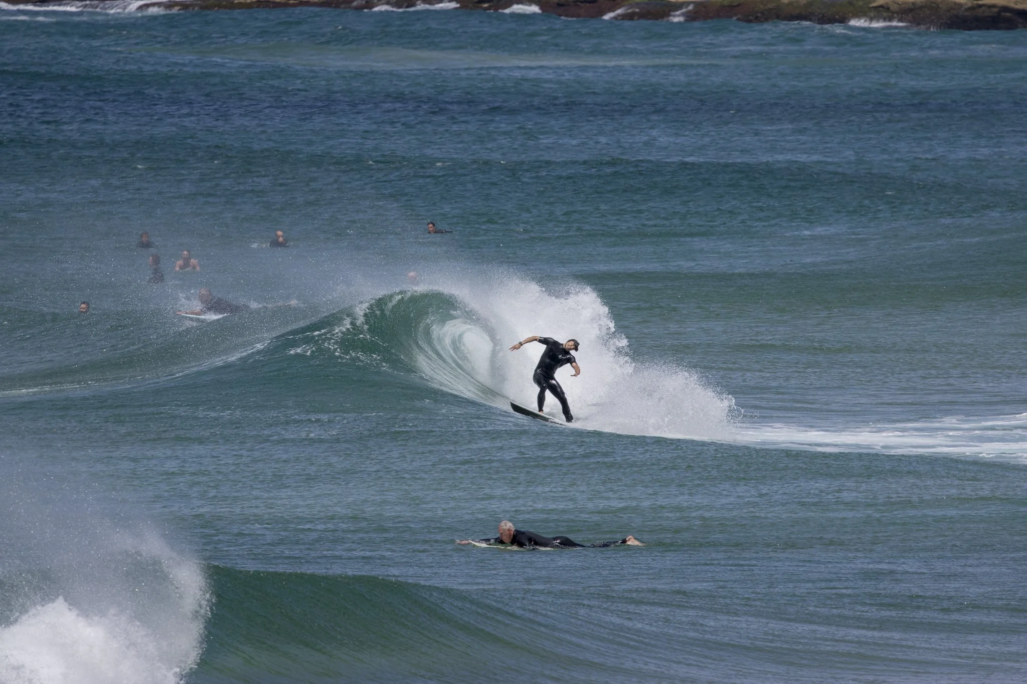 A person surfing on a wave in the ocean with other surfers and swimmers in the background.