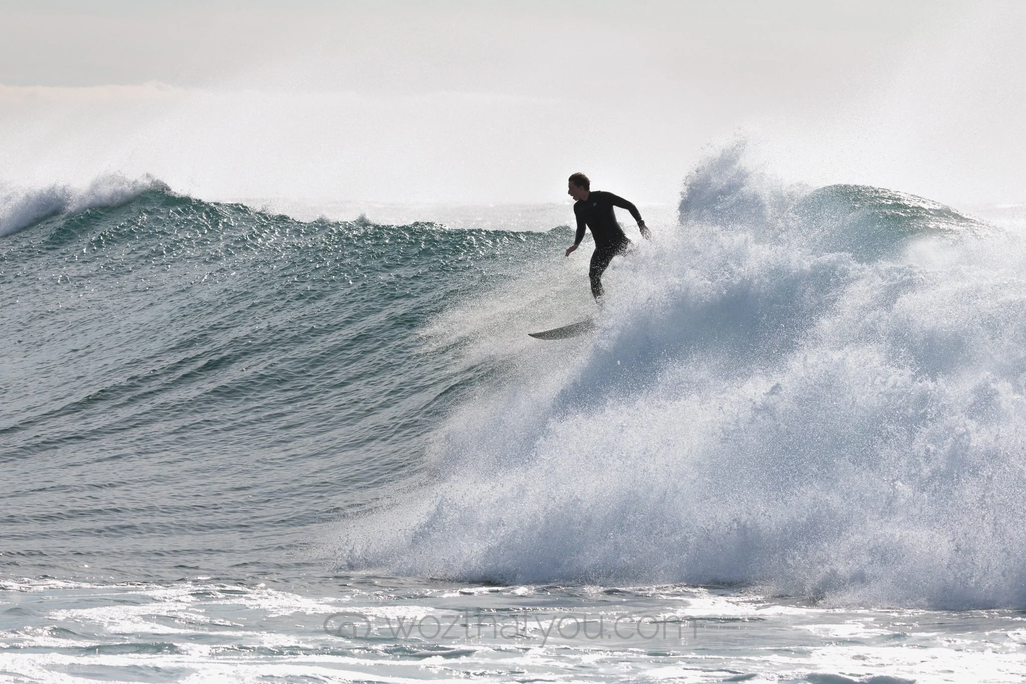A person surfing on a wave in the ocean, wearing a black wetsuit.