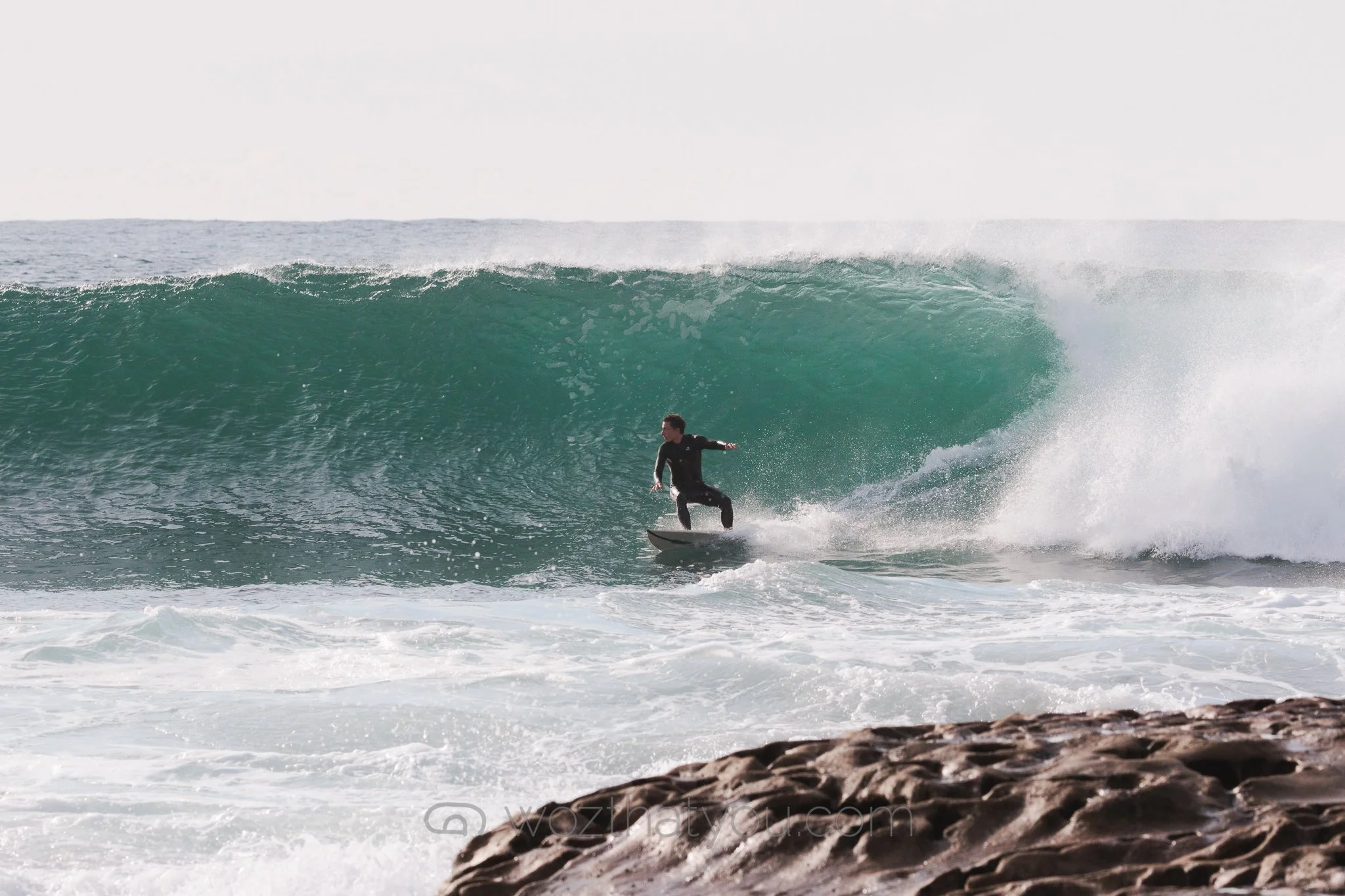 A person surfing on a wave near the rocky shoreline.