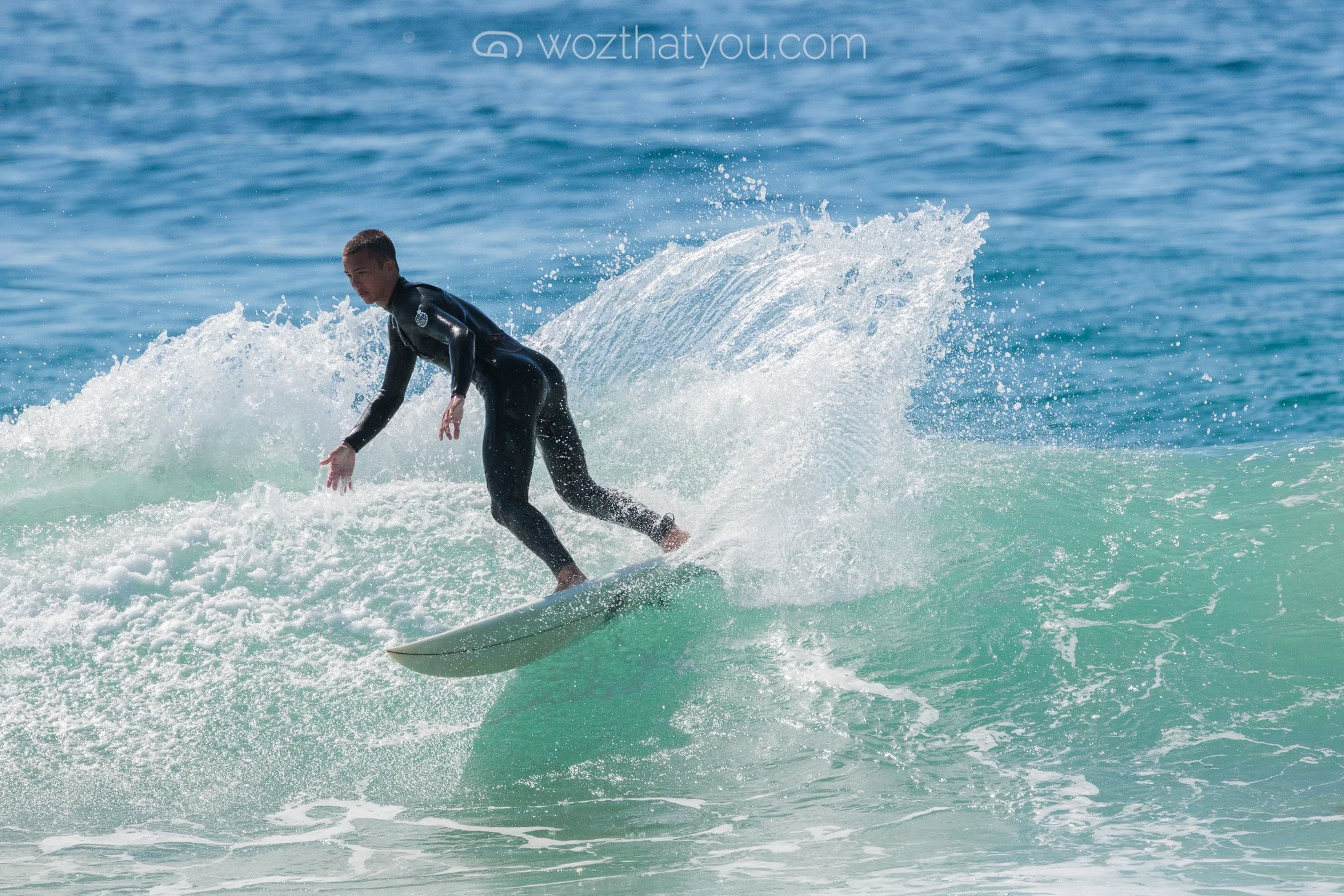 A person surfing on a wave in the ocean, wearing a black wet suit.