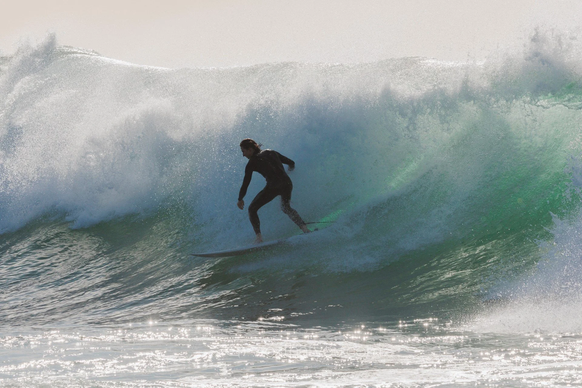 Person surfing on a wave in the ocean with sunlight reflecting off the water.