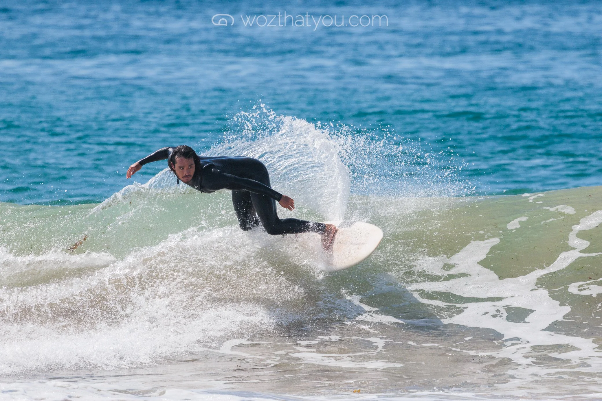 A person in a black wetsuit surfing on a wave at the beach.