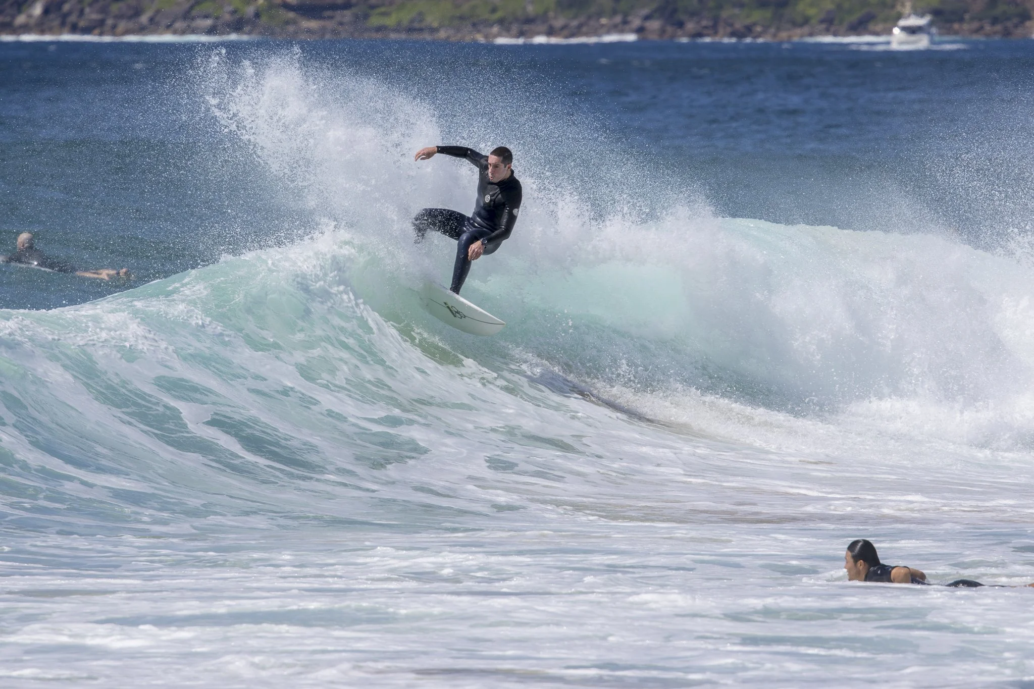 A man surfing on a wave in the ocean, with a person swimming nearby.