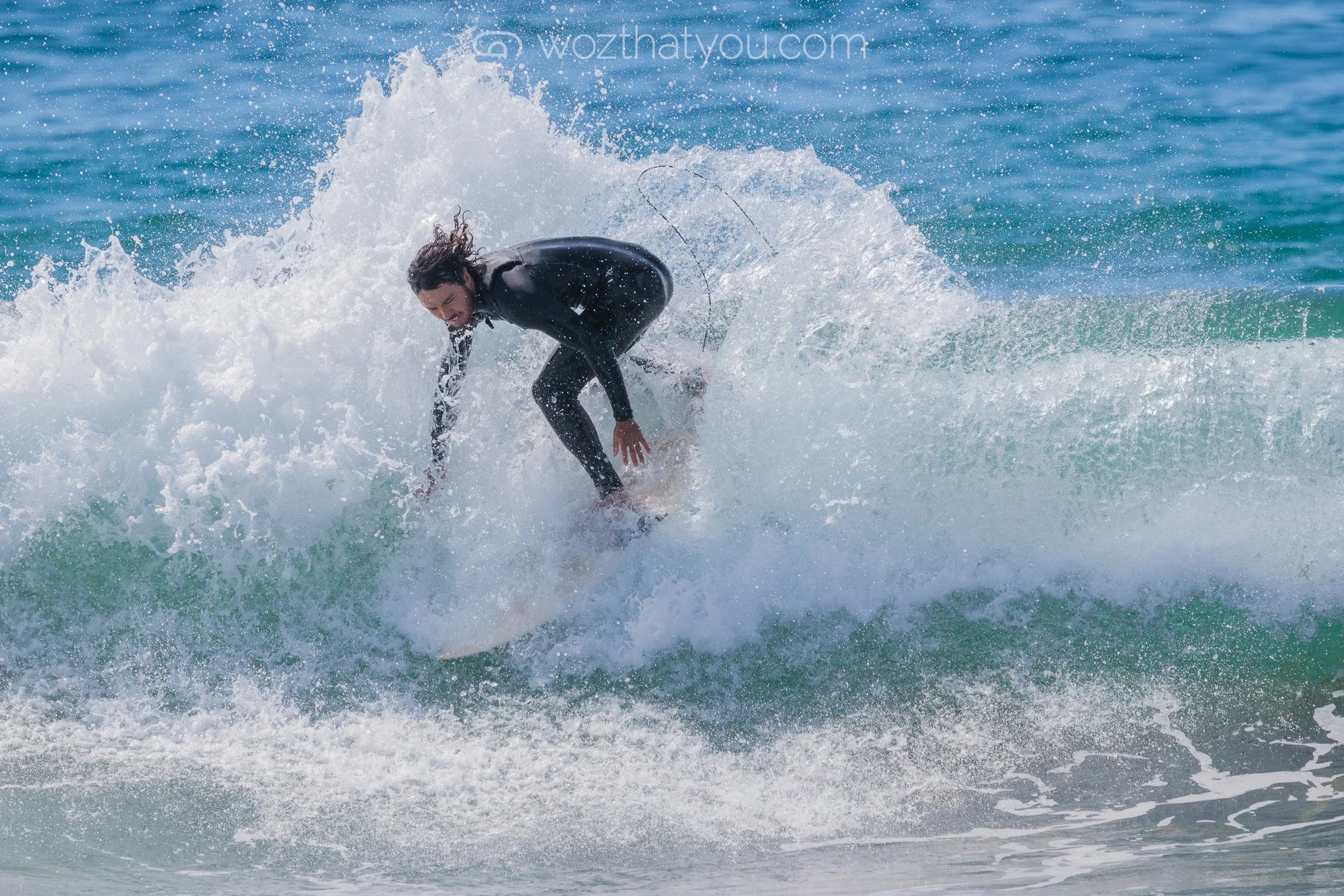 Person surfing on a wave in the ocean, wearing a wetsuit and with long hair flowing back.