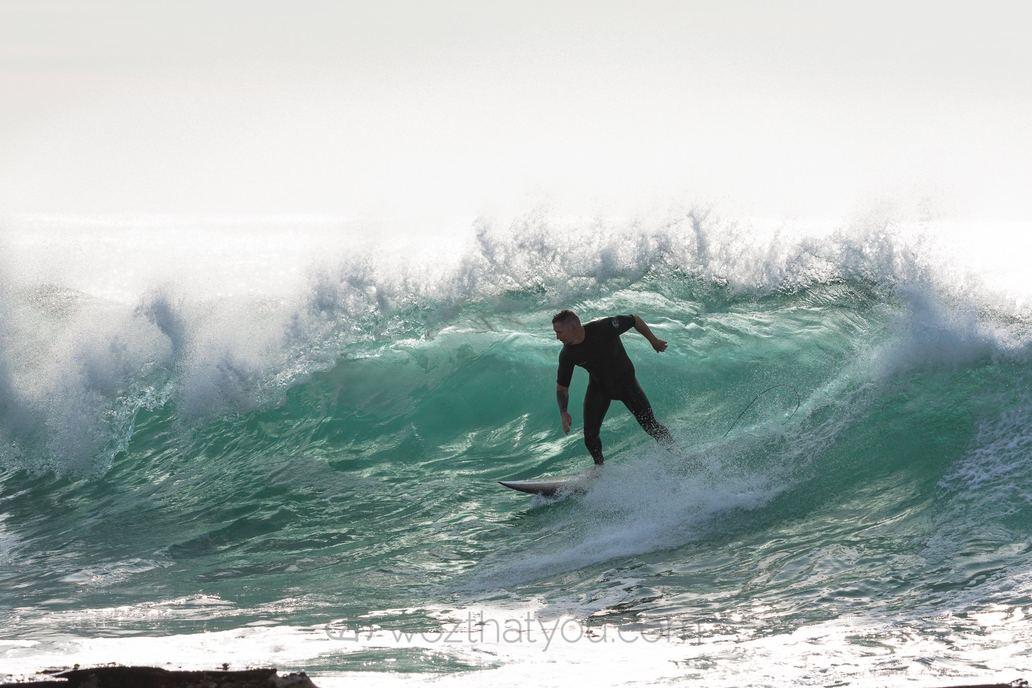 Surfer riding a wave with a clear sky in the background.