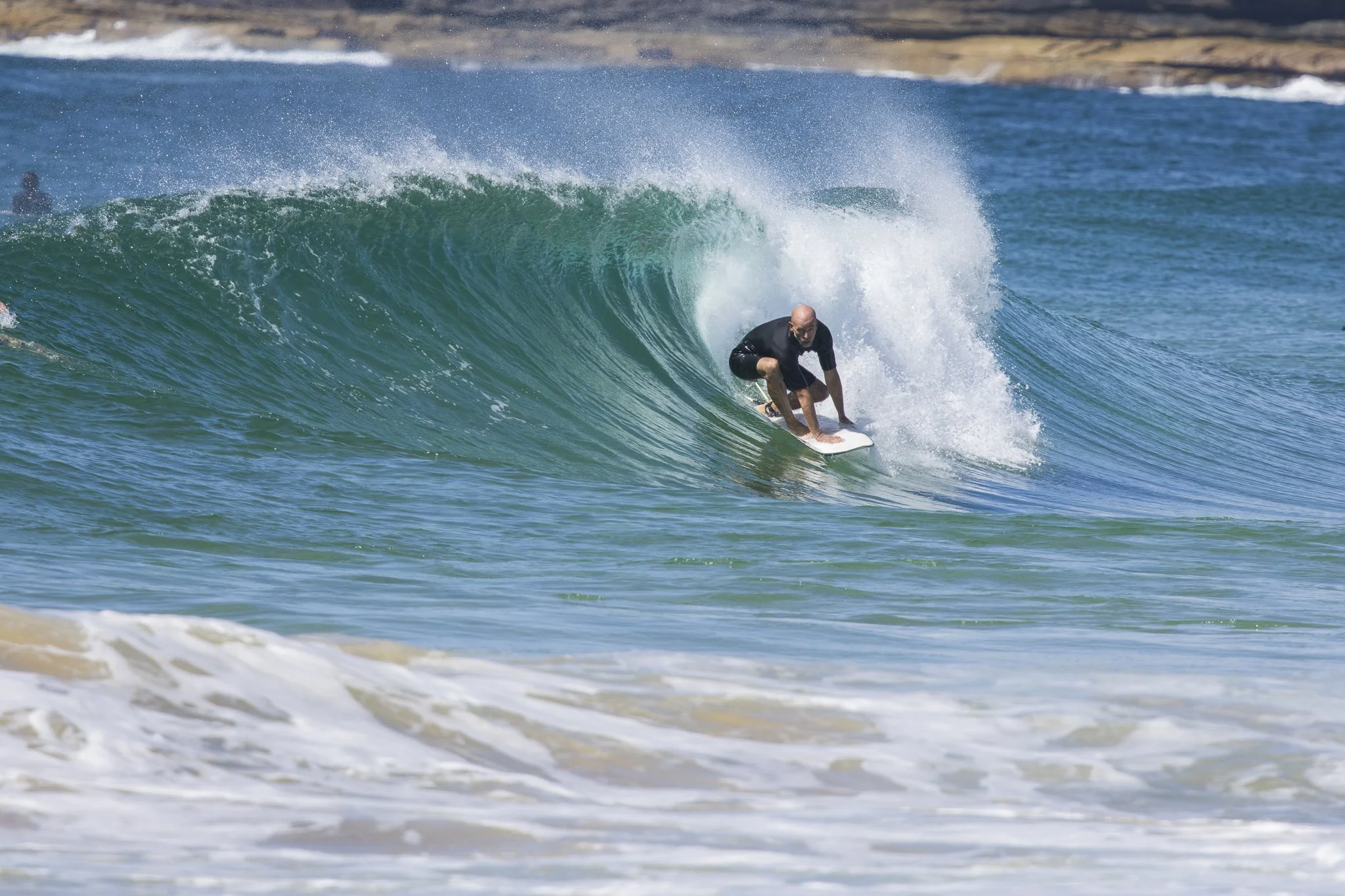 A man surfing a large turquoise wave in the ocean.