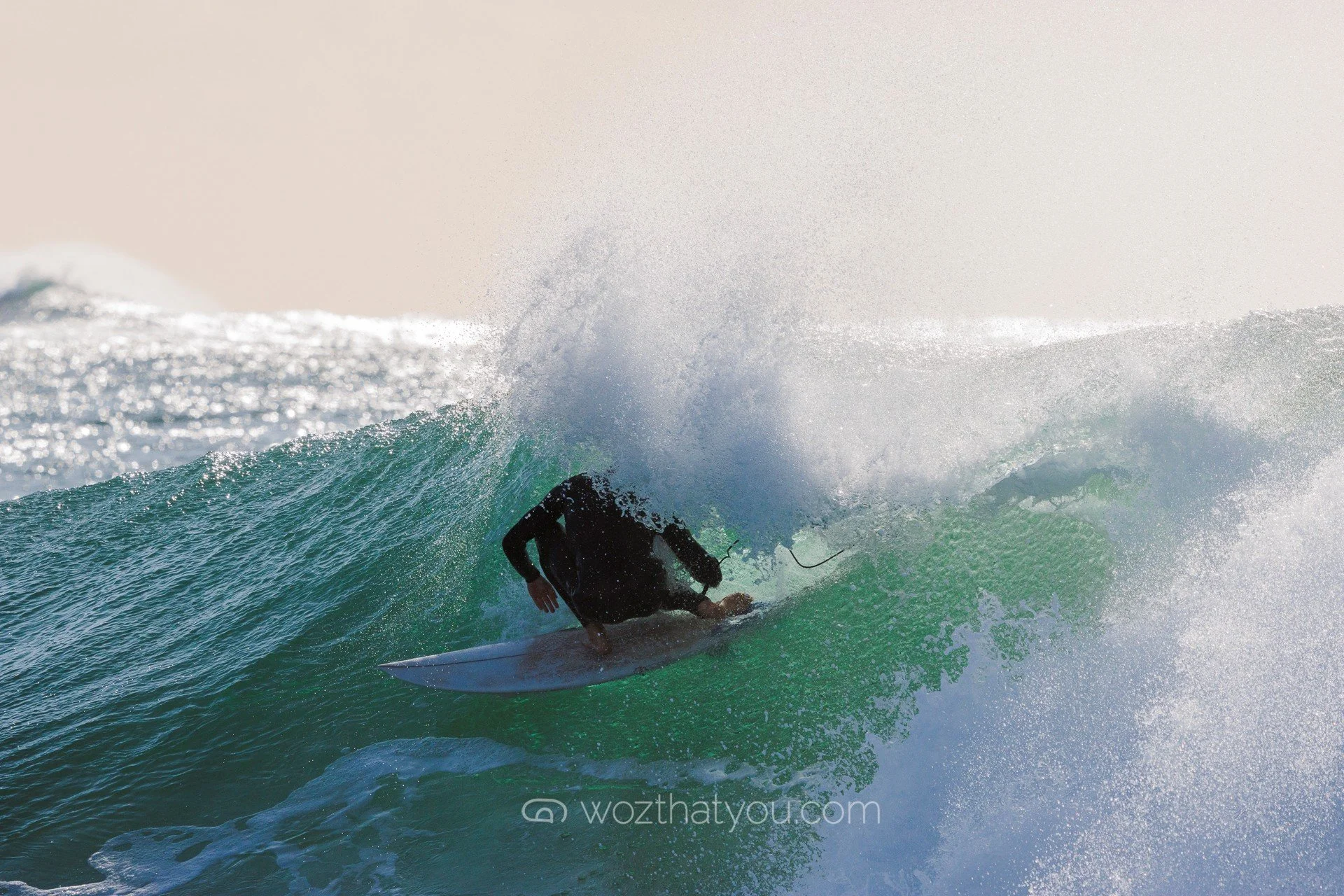 A person in black clothing is surfing inside a large, curling wave.