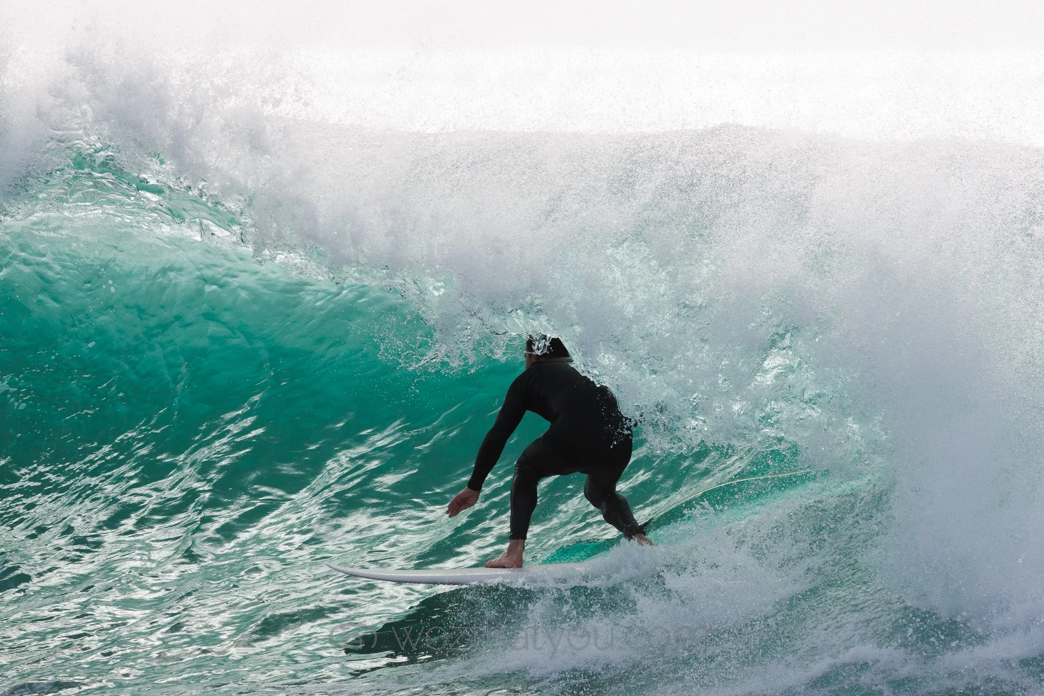 A person surfing on a wave in the ocean, wearing a black wetsuit, with water splashing around.
