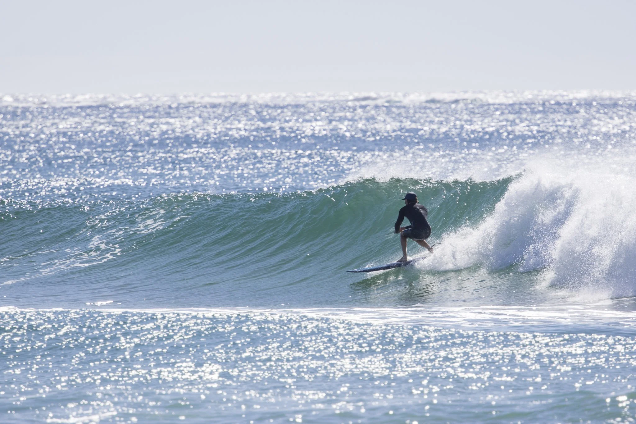 A person surfing on a wave in the ocean with sunlight reflecting off the water.