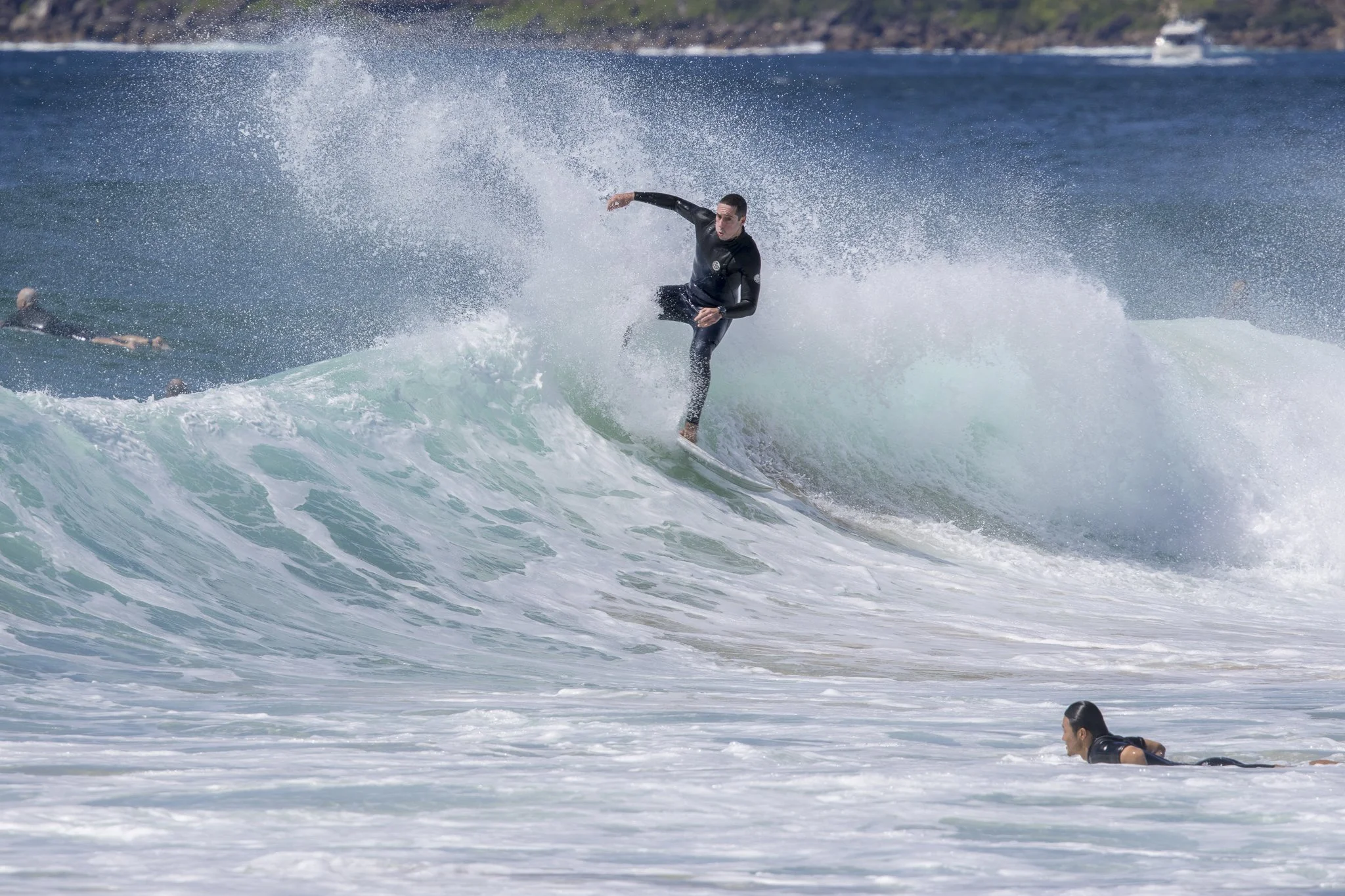 A man surfing on a wave while another person paddles in the water nearby in the ocean.