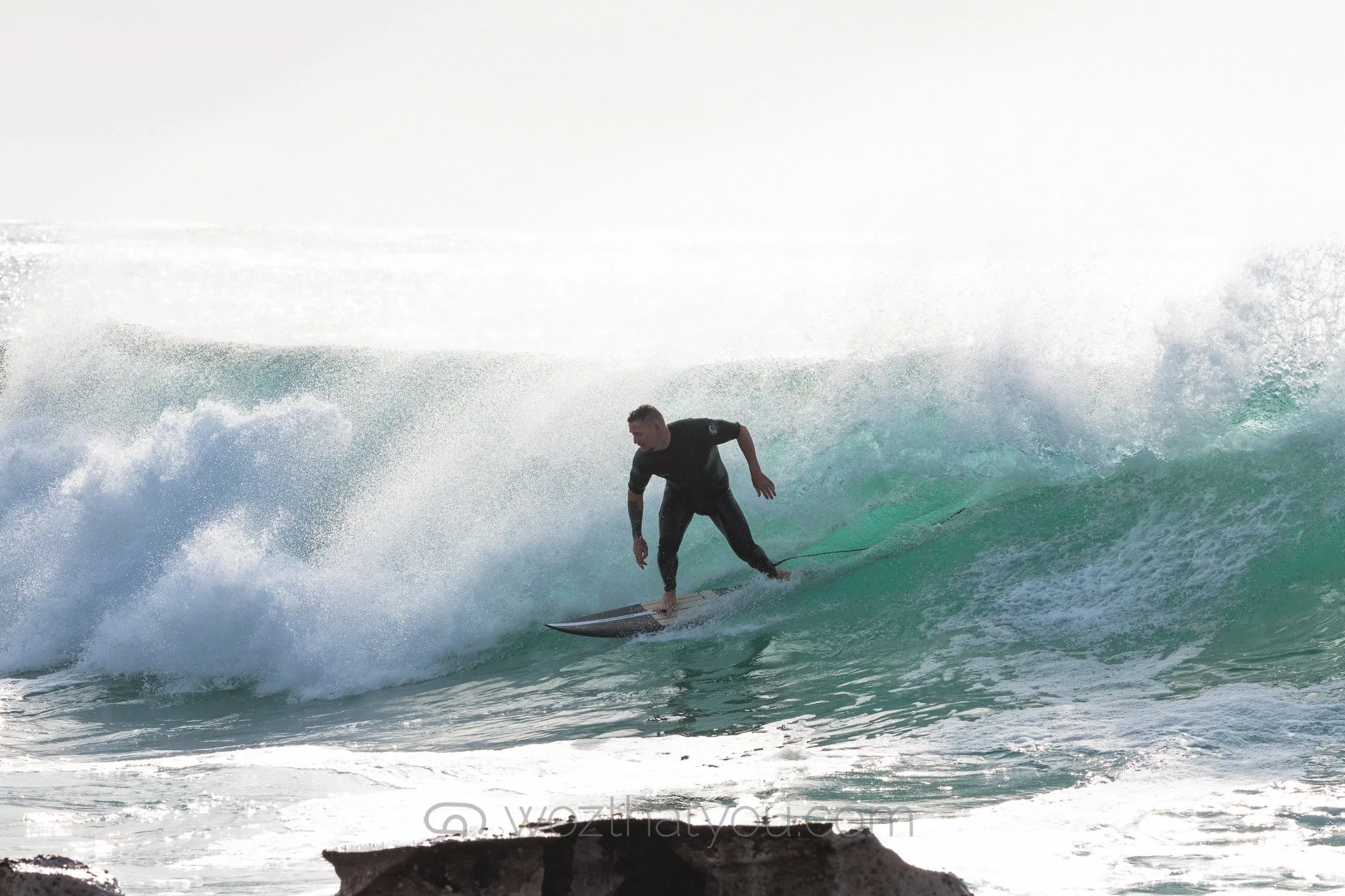 A man surfing on a wave in the ocean, wearing a black wetsuit.