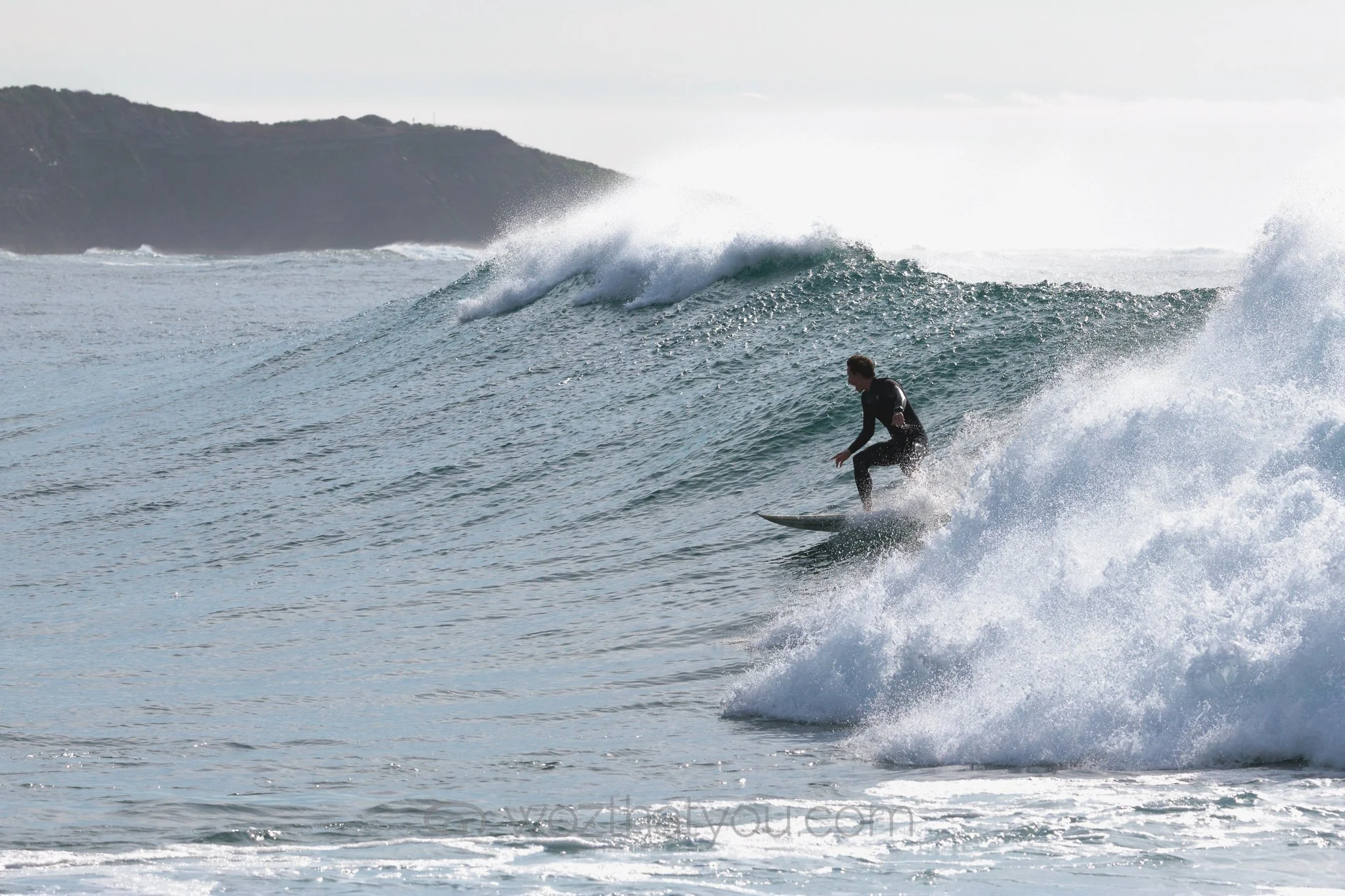 A surfer riding a wave in the ocean with a distant landmass in the background.