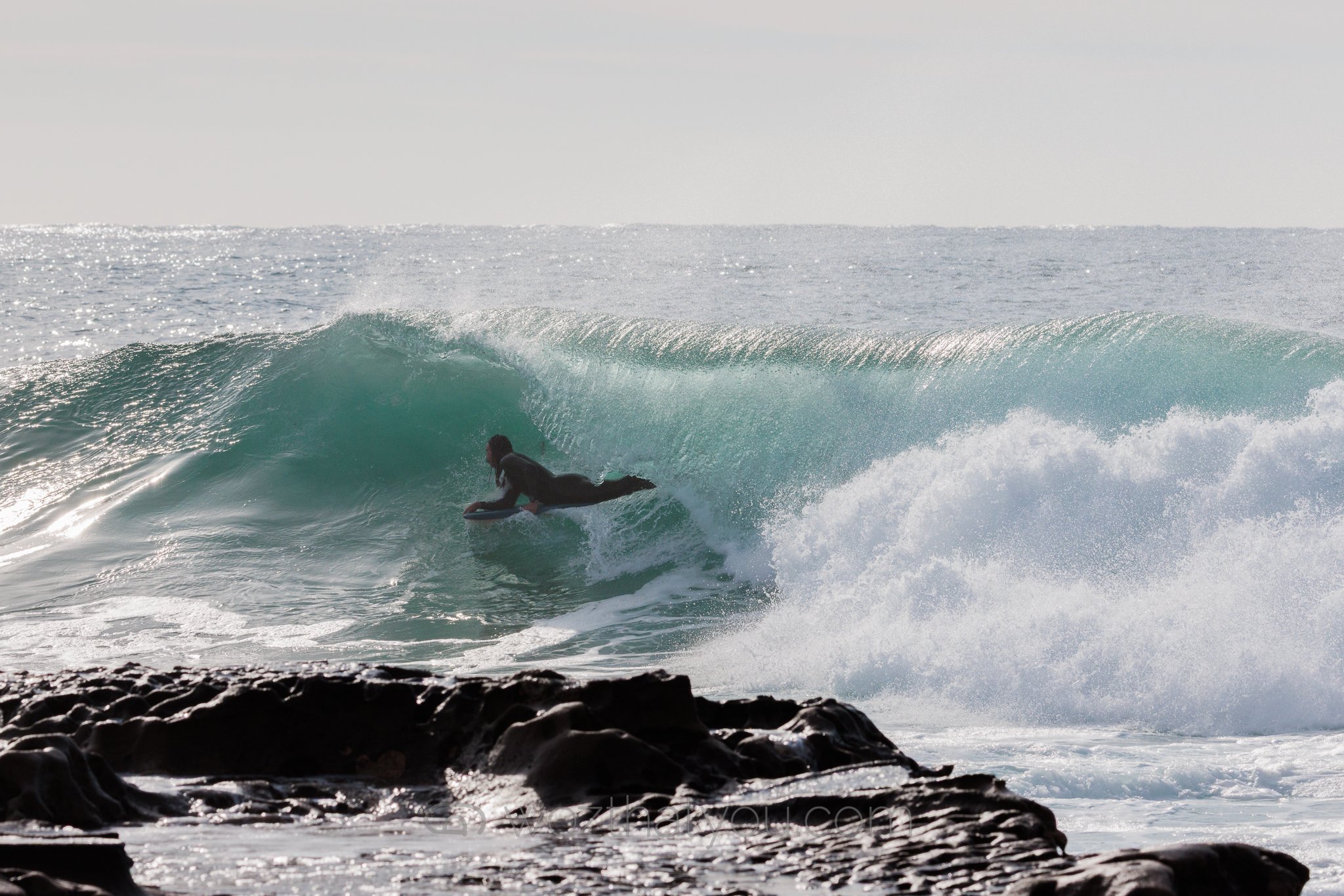 A person surfing on a wave near a rocky shoreline.