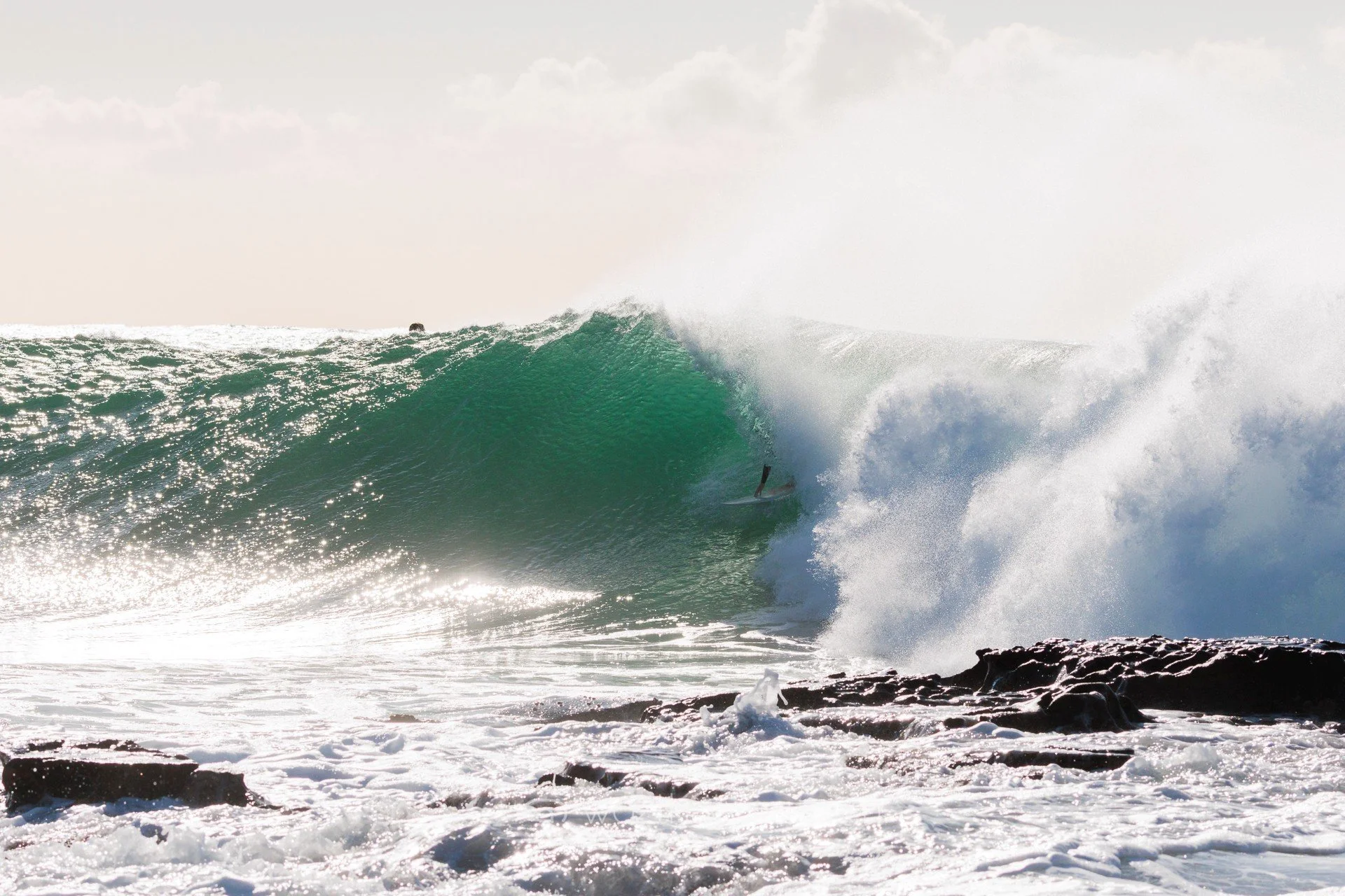 A surfer riding inside the barrel of a large ocean wave near a rocky shoreline.