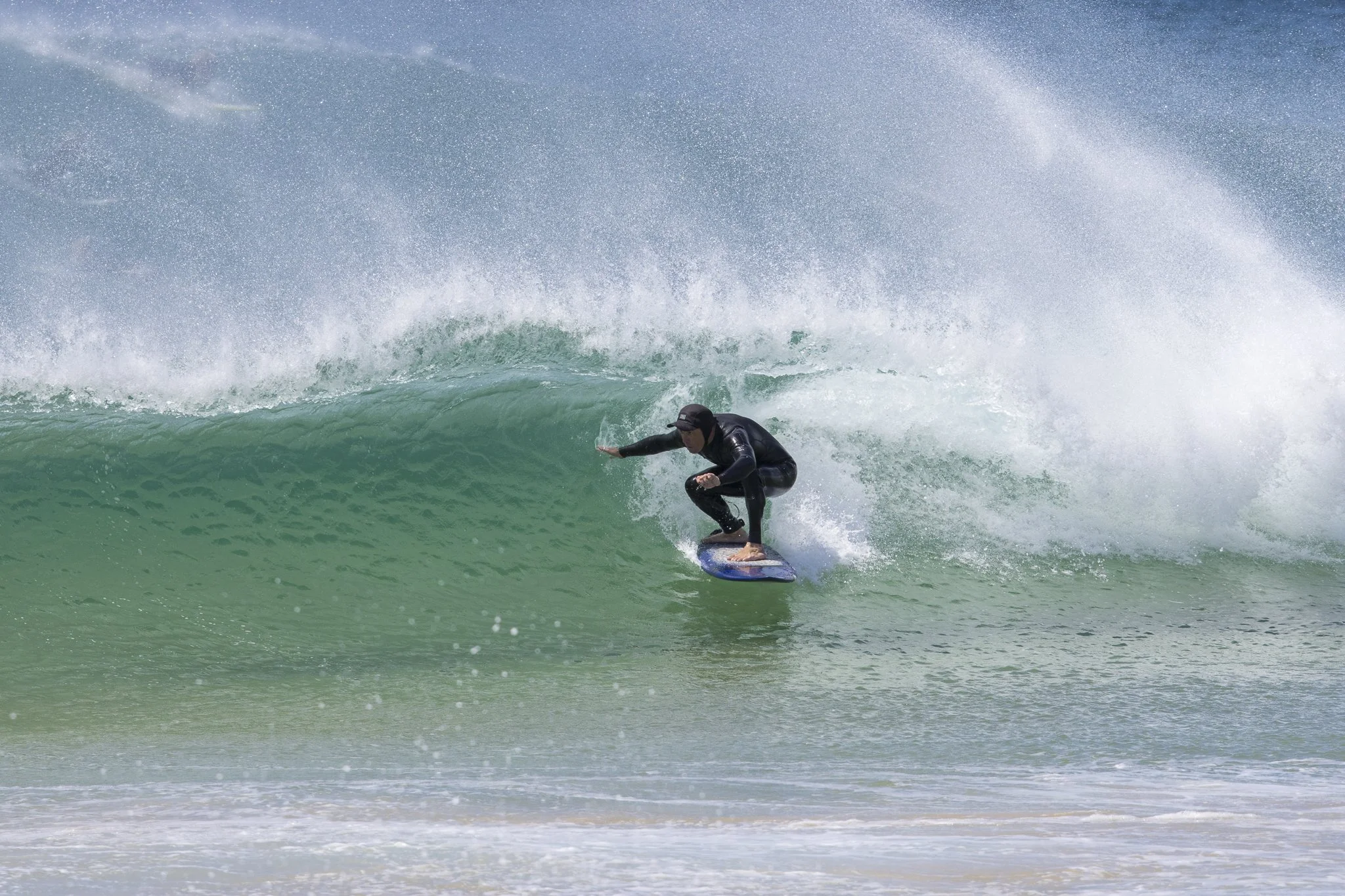 A person wearing a wetsuit and helmet riding a surfboard inside a large green wave at the beach.