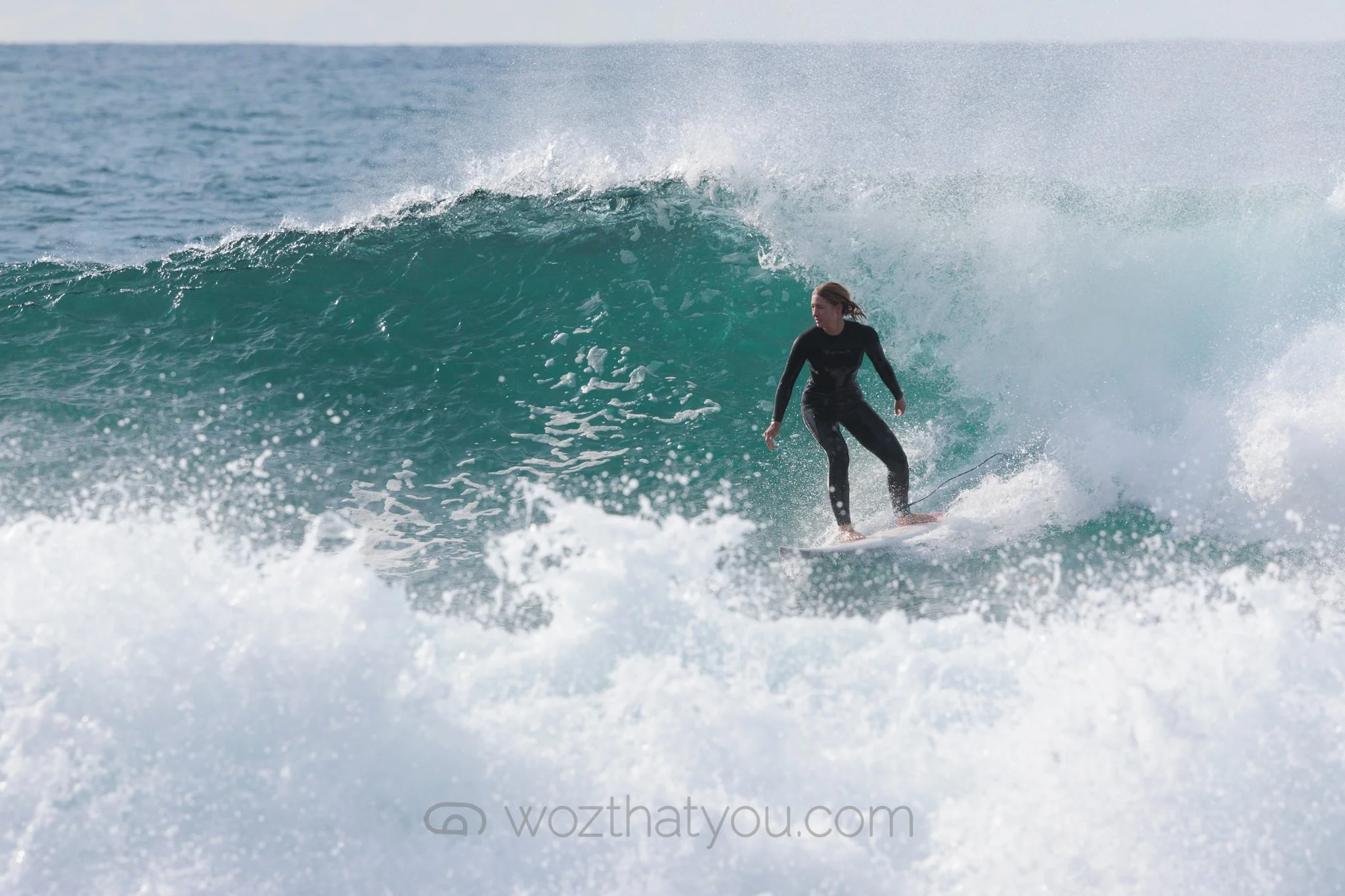 A person surfing on a wave in the ocean, wearing a wetsuit.