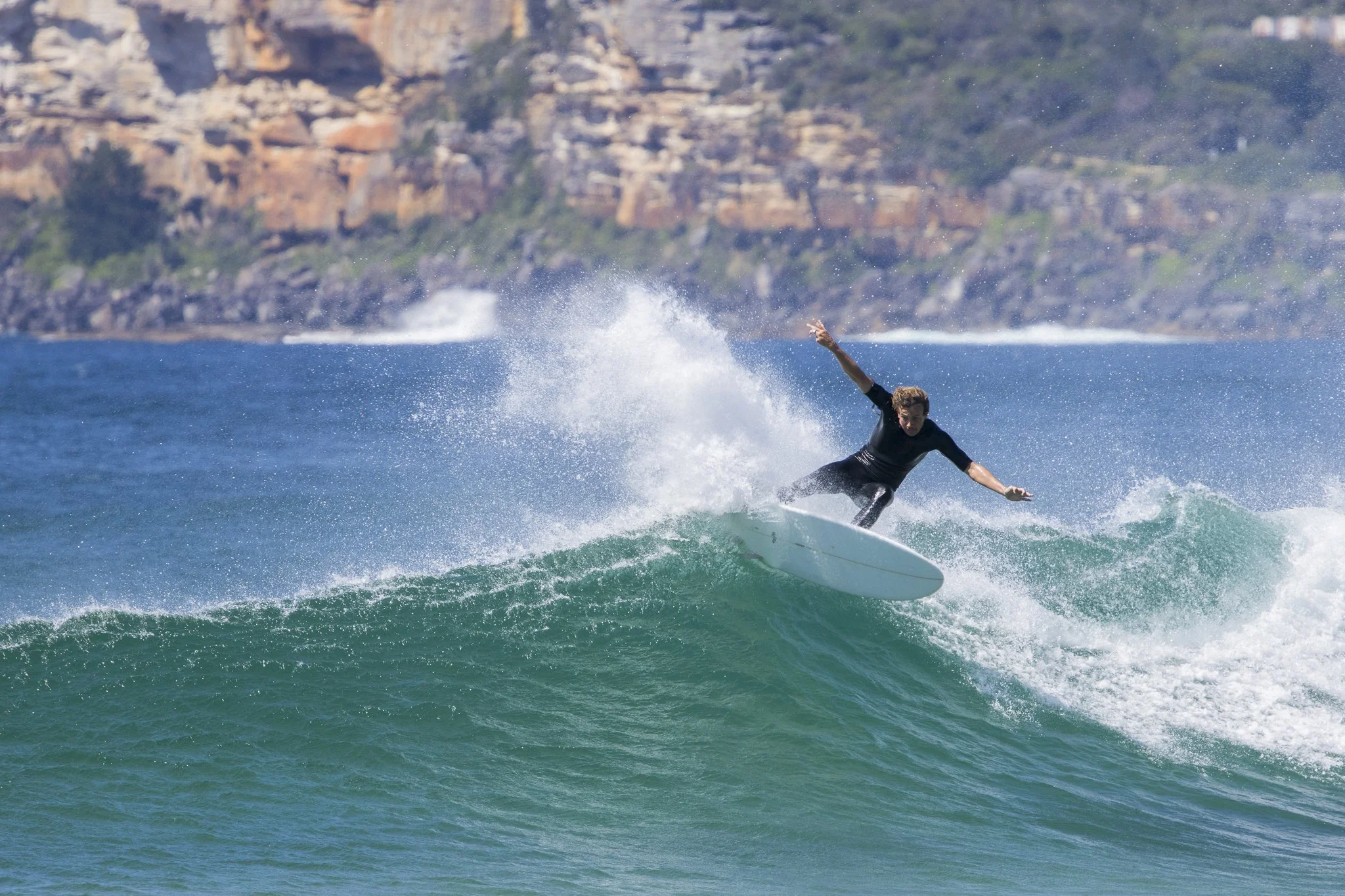 A person surfing on a wave in the ocean with rocky cliffs in the background.