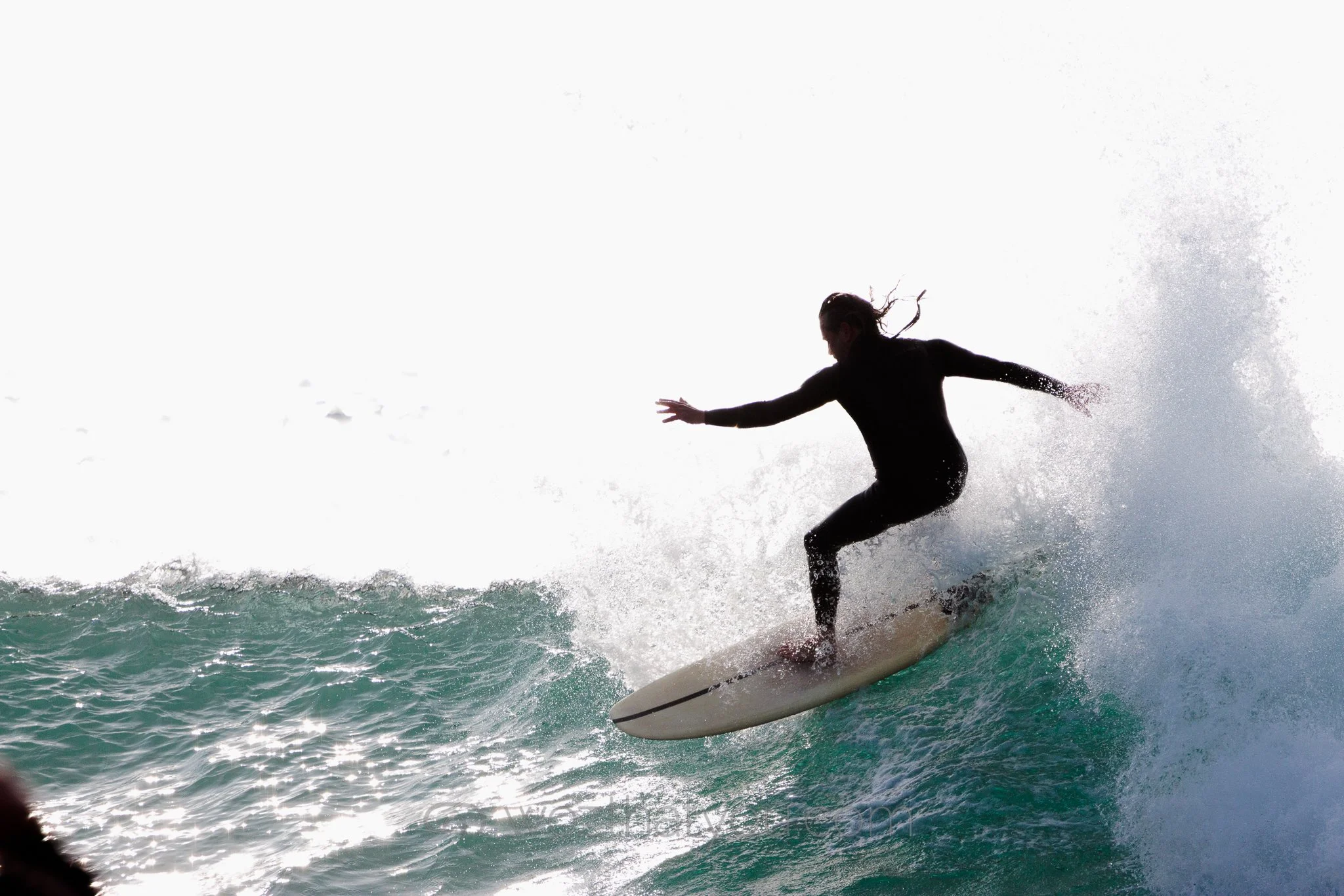 A person in black clothing surfing on a wave in the ocean, with spray and water splashing around.