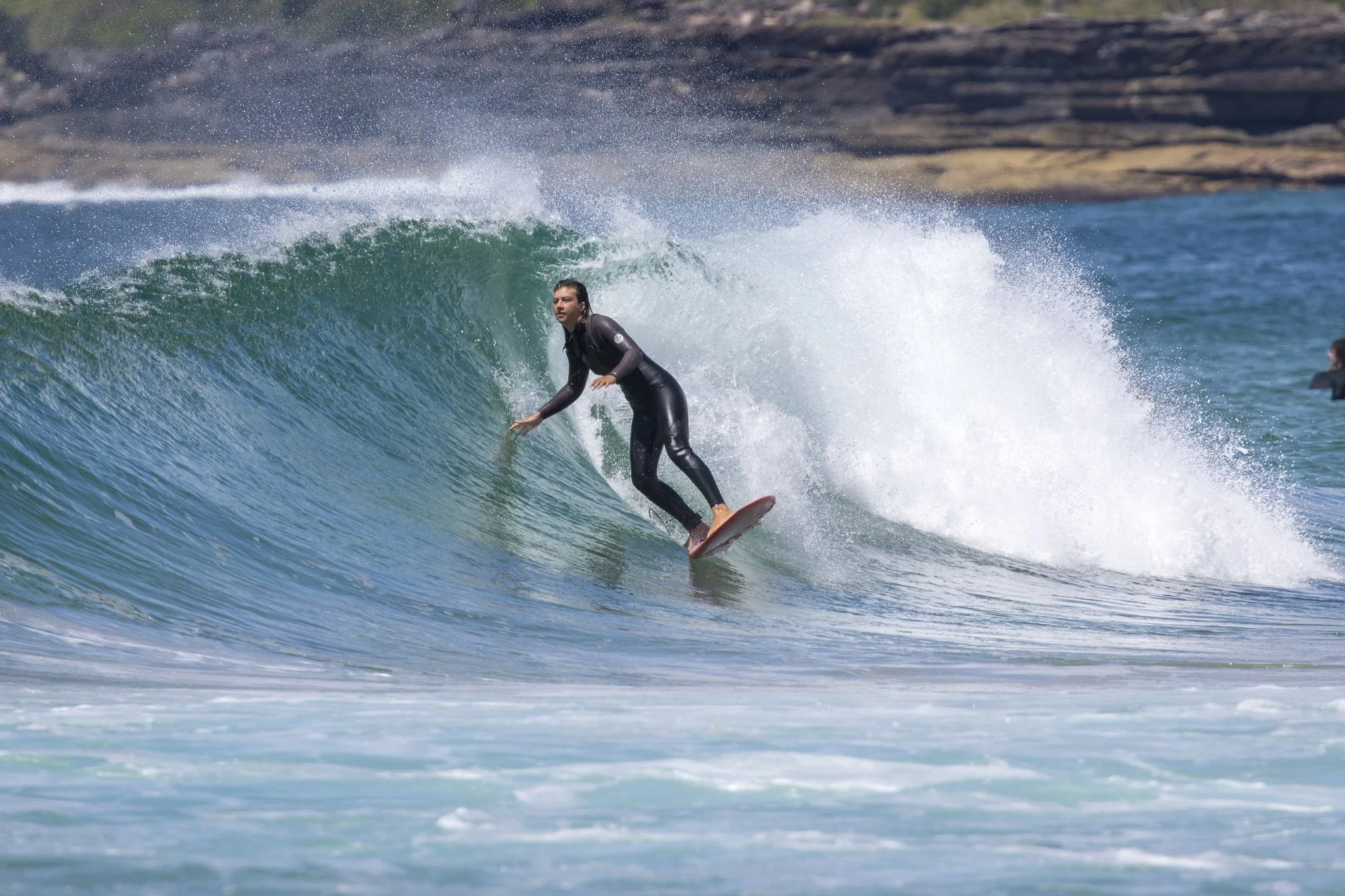 A woman surfing on a large wave at the beach, wearing a black wetsuit.
