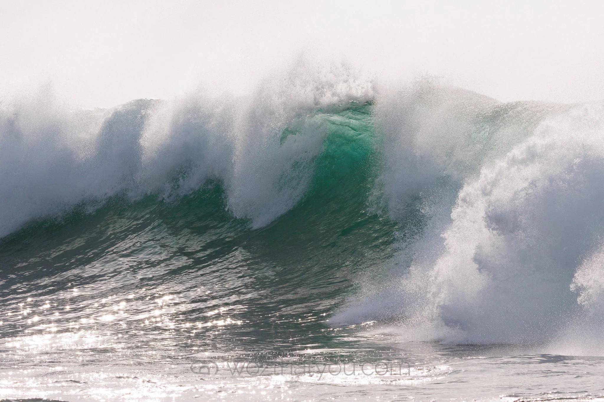 A large ocean wave crashing with water splashing and foam in the air.