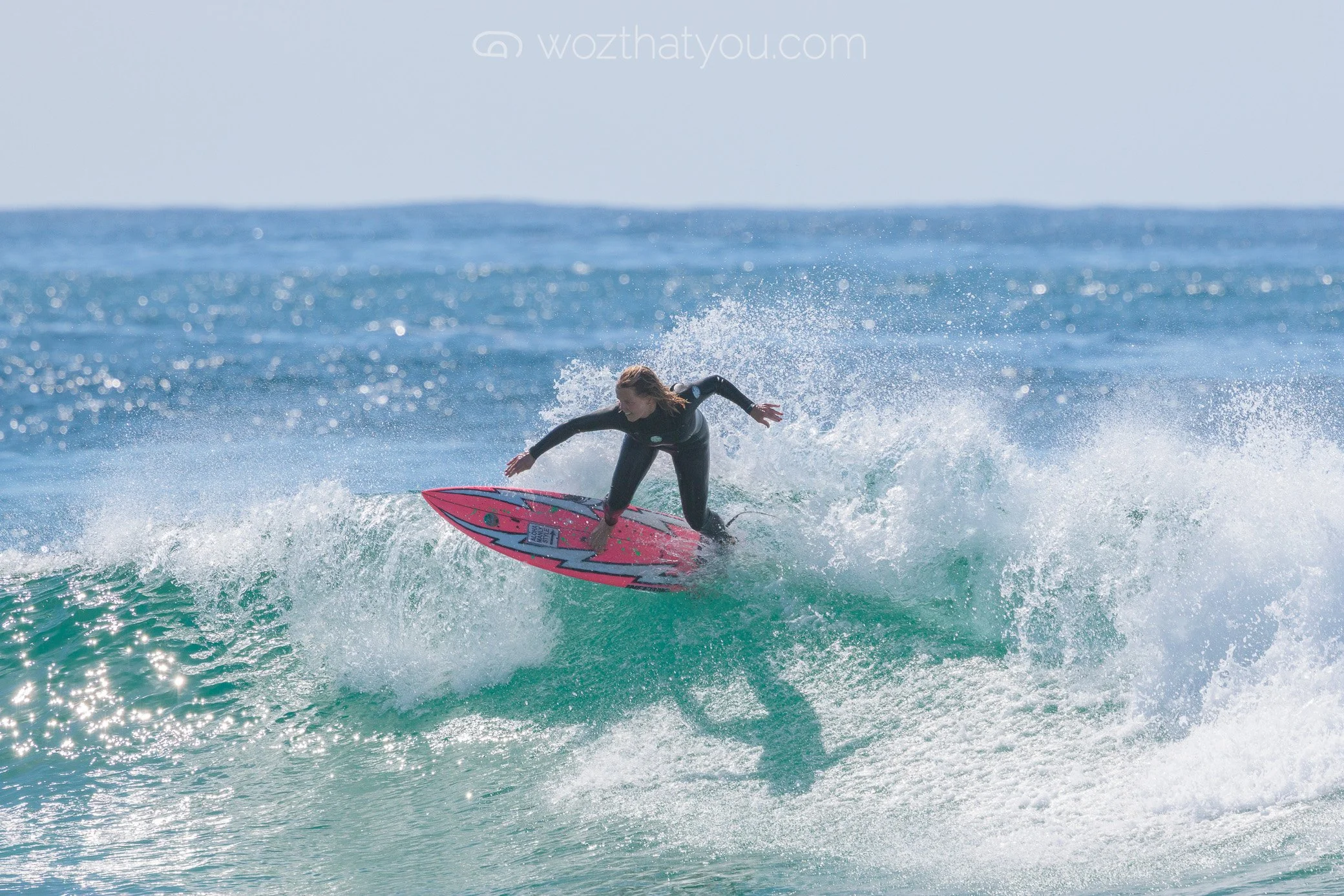 A woman riding a wave on a pink surfboard in the ocean.