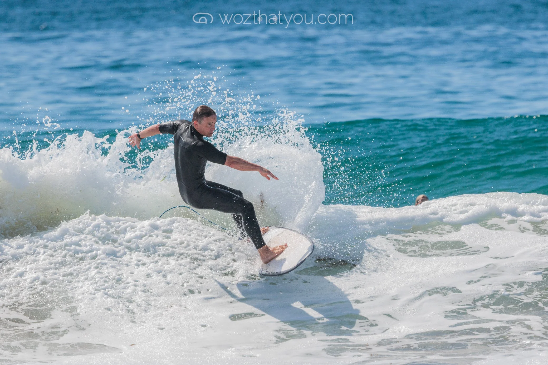 A man surfing on a wave in the ocean under a clear sky.